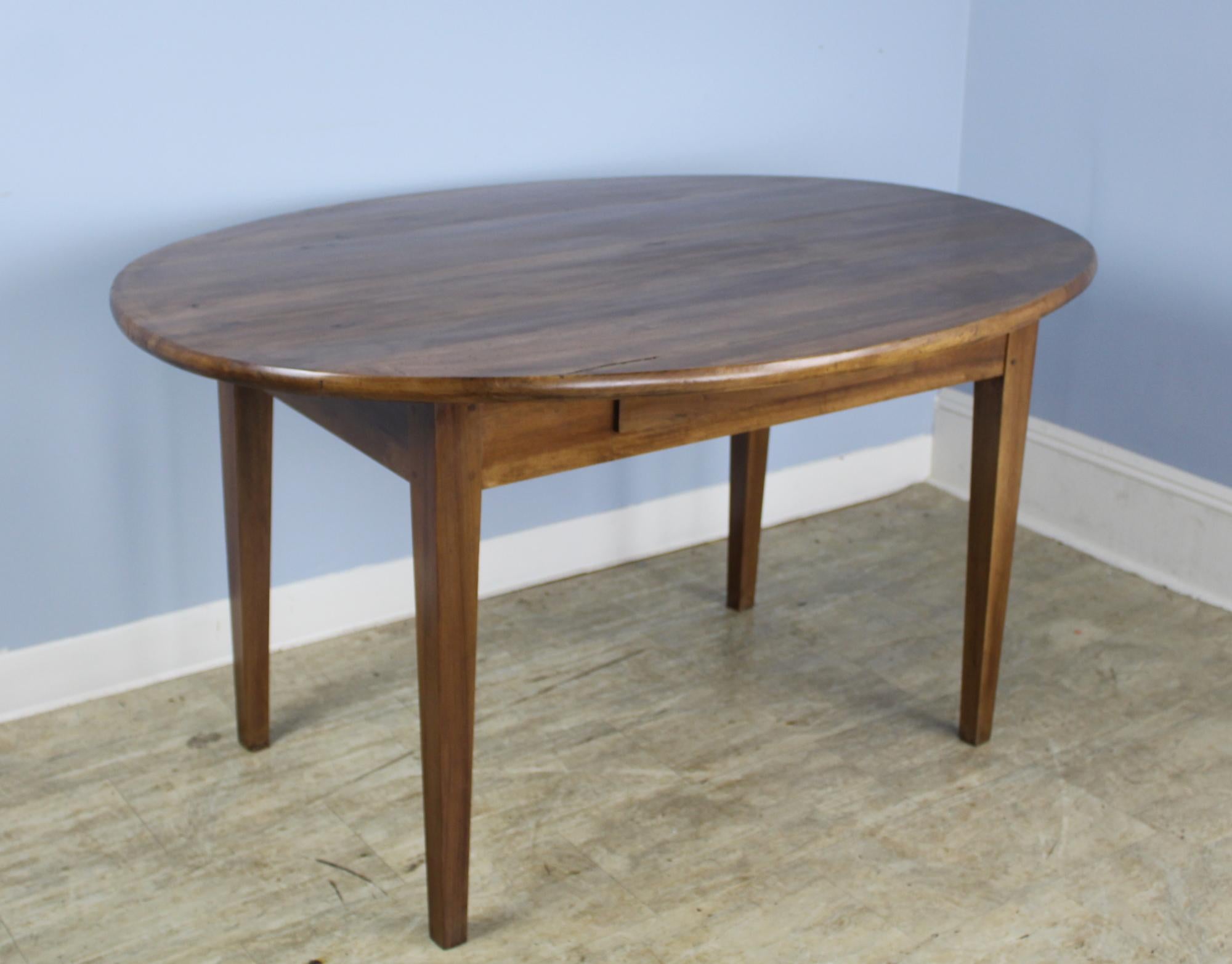 A simple and elegant oval dining table in mellow fruitwood with warm patina. The thick top is pretty and in good condition, nicely pegged at the legs. Apron height is 23 inches; the base is inset for seating comfort. There are a few small areas of