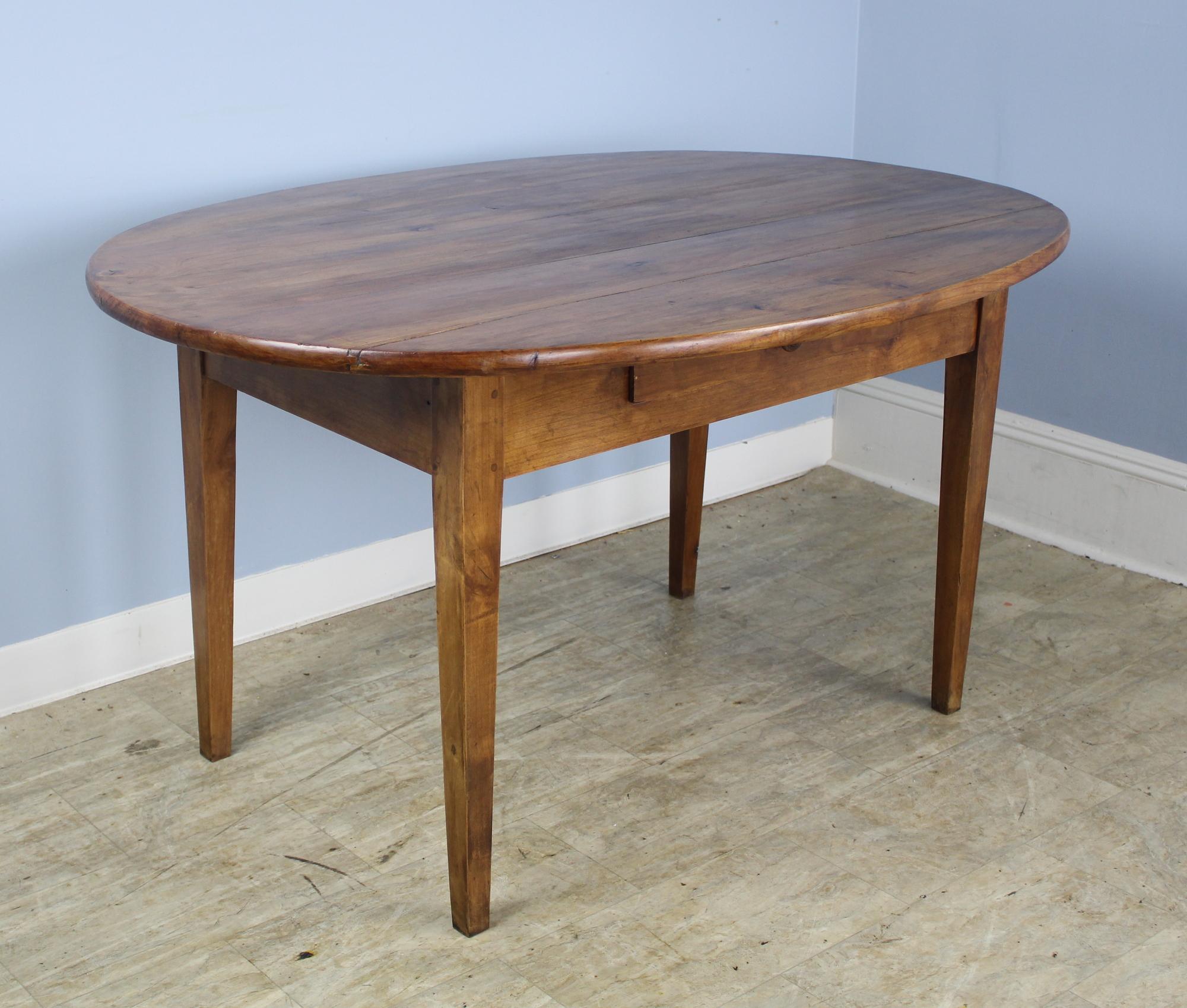 A simple and elegant oval dining table in mellow fruitwood with warm patina. The thick top is pretty and in good condition, nicely pegged at the legs. Apron height is 23 inches; the base is inset for seating comfort. There are a few interesting