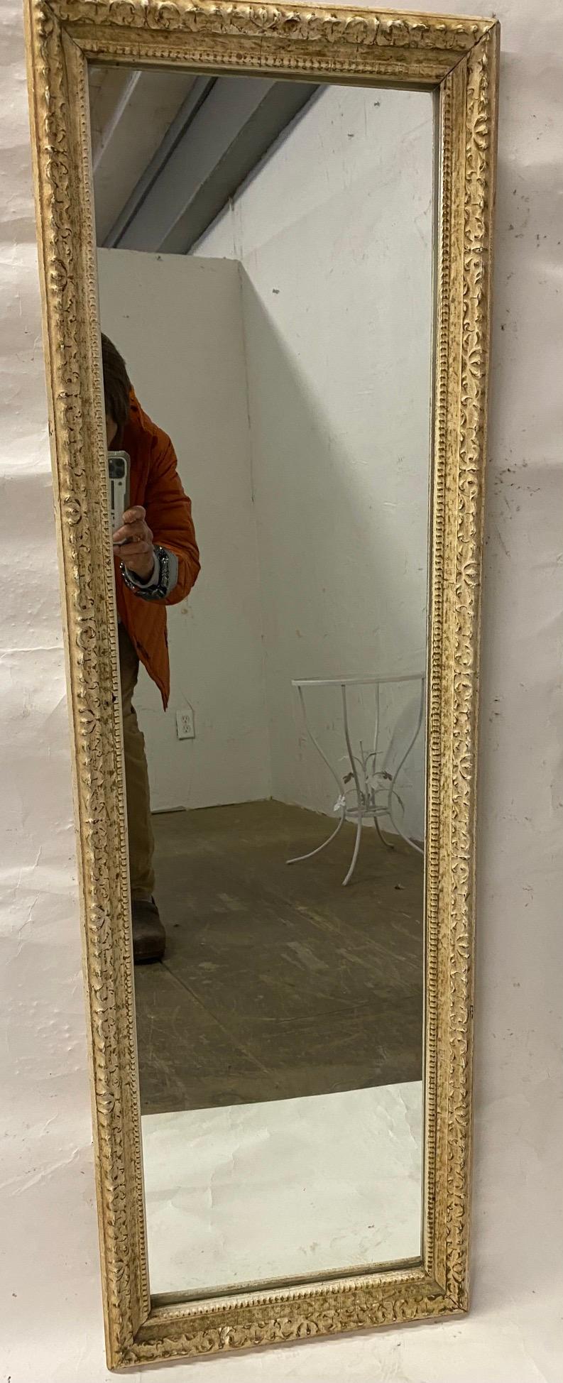 A slender and tall antique French wall mirror with scrollwork design.