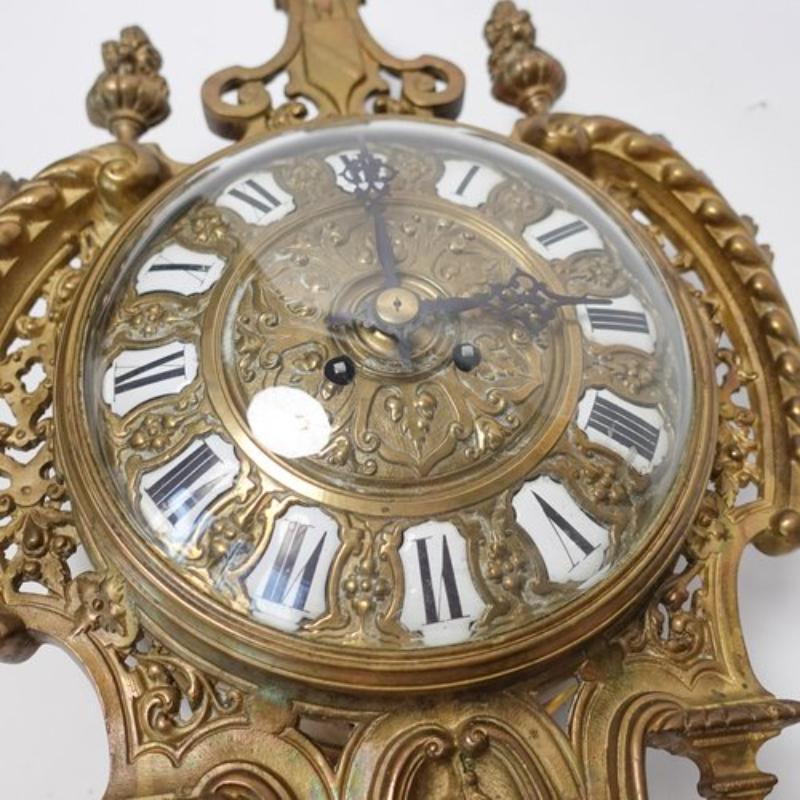 French clockmakers were renowned for their craftsmanship during the 19th century. 
An antique framed hanging Cartel wall clock made of gilded bronze. The hours are shown as Roman numerals. It comes with a round glass cover in the front to protect
