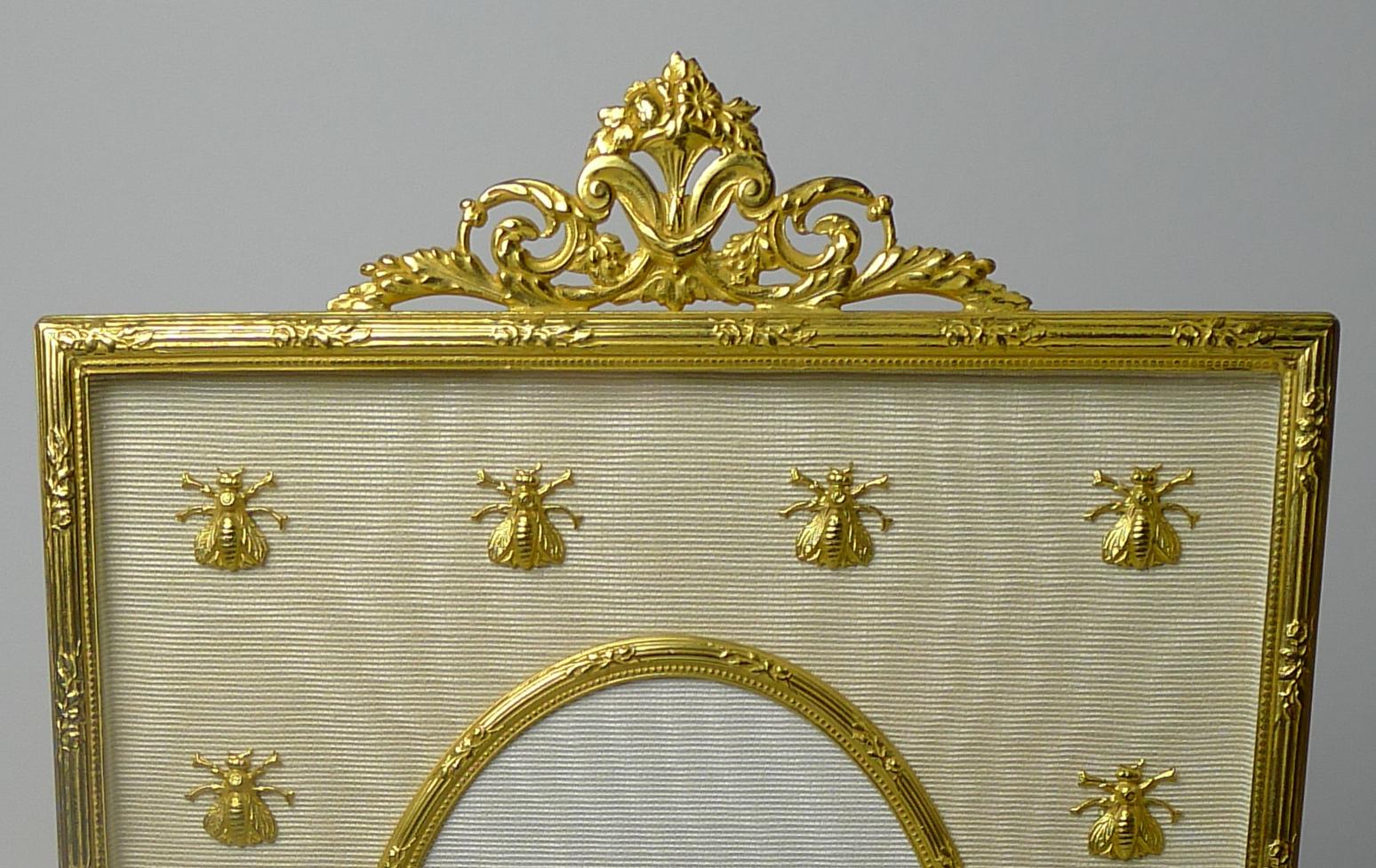 Always highly sought-after, this bronze dore photograph frame is lucky enough to be decorated with a series of gilded bronze bees mounted onto the cream coloured silk taffeta.  The central oval aperture measures 4 1/2