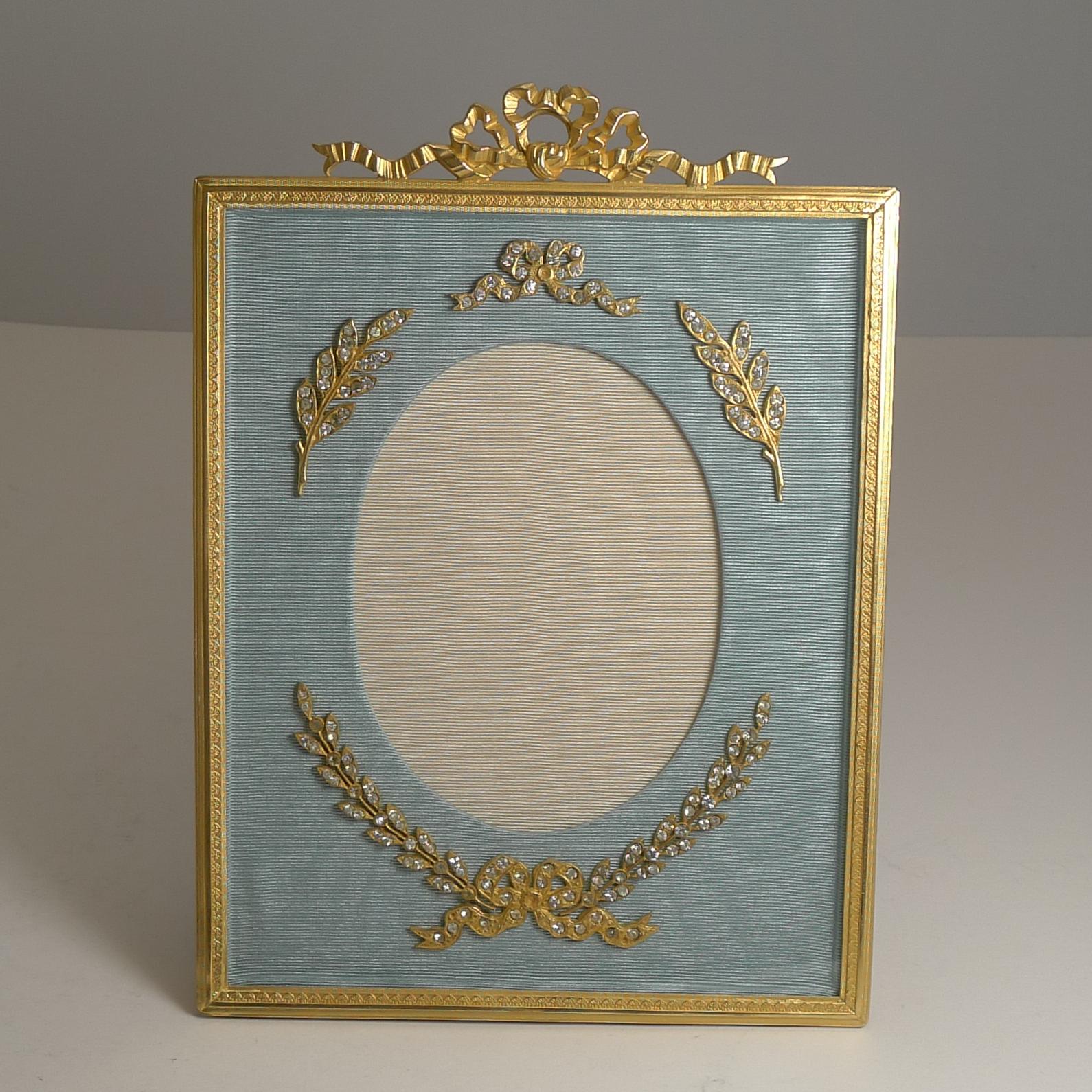A stunning antique French gilded bronze / Ormolu picture frame beautifully restored to it's former glory.

The top is crowned with a ribbon and bow mount and behind the glass are stunning bronze mounts set with period paste stones sitting on an eau