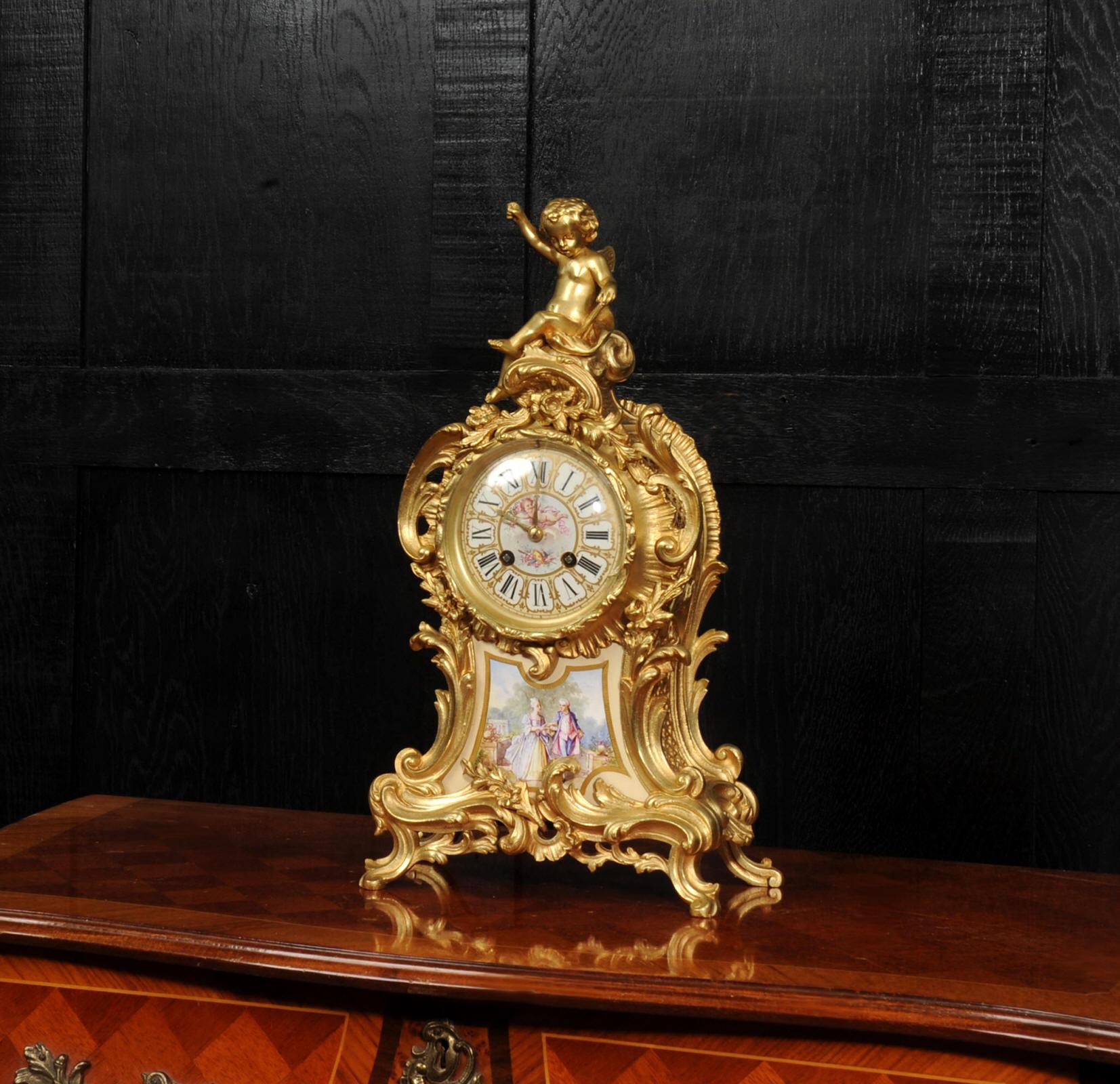 A highly decorative and beautifully modelled French gilt-bronze mantel clock, of elegant Louis XV Rococo revival design, surmounted by an exceptionally charming putto. Set within the sweeping gilt-bronze scrollwork is a finely painted Sèvres style