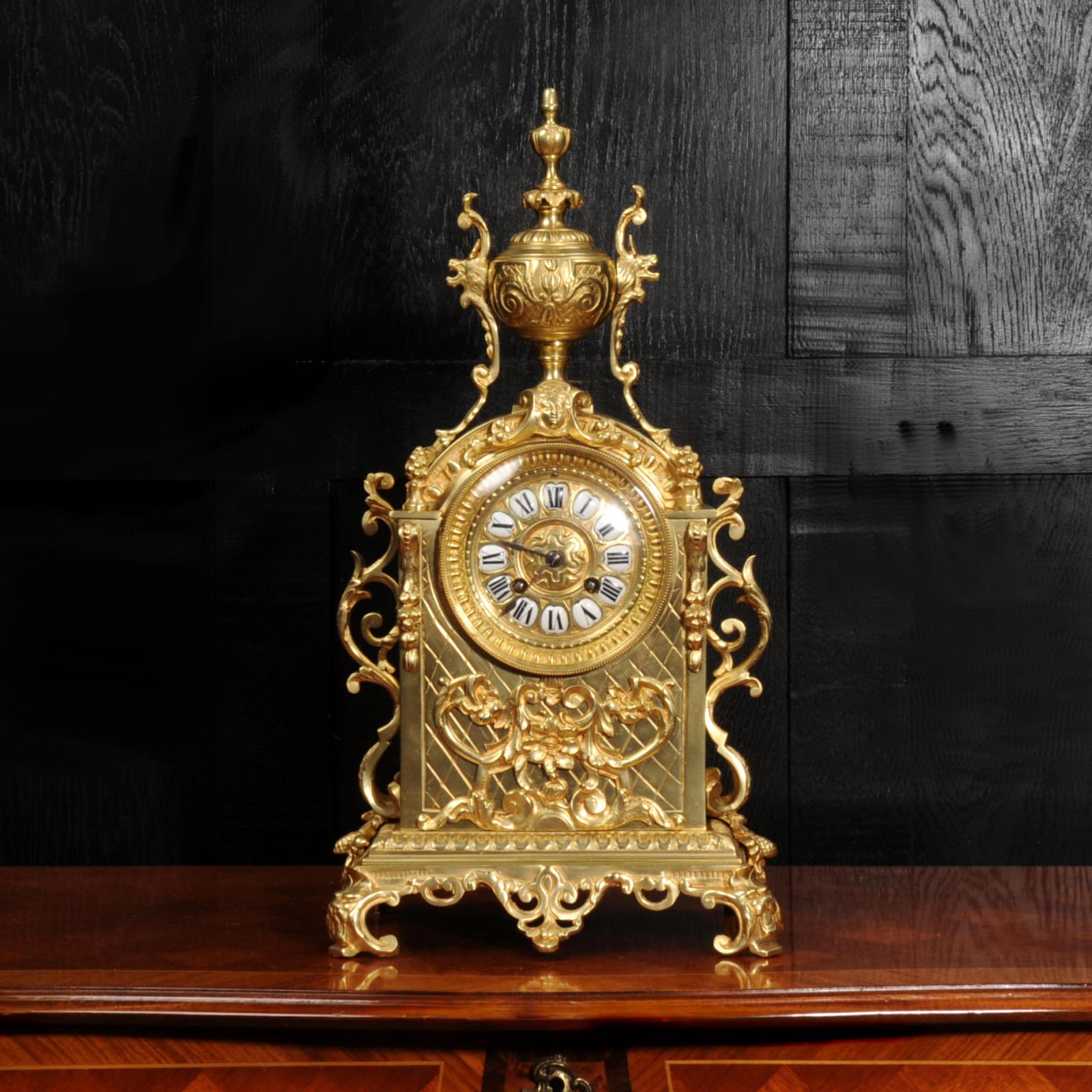 A beautiful original antique French clock, modelled in the Baroque style in gilt bronze. It is of architectural form with an applied motif of flowers, scrolls and cornucopia. Scrolling brackets are mounted to the sides and an urn with mythical