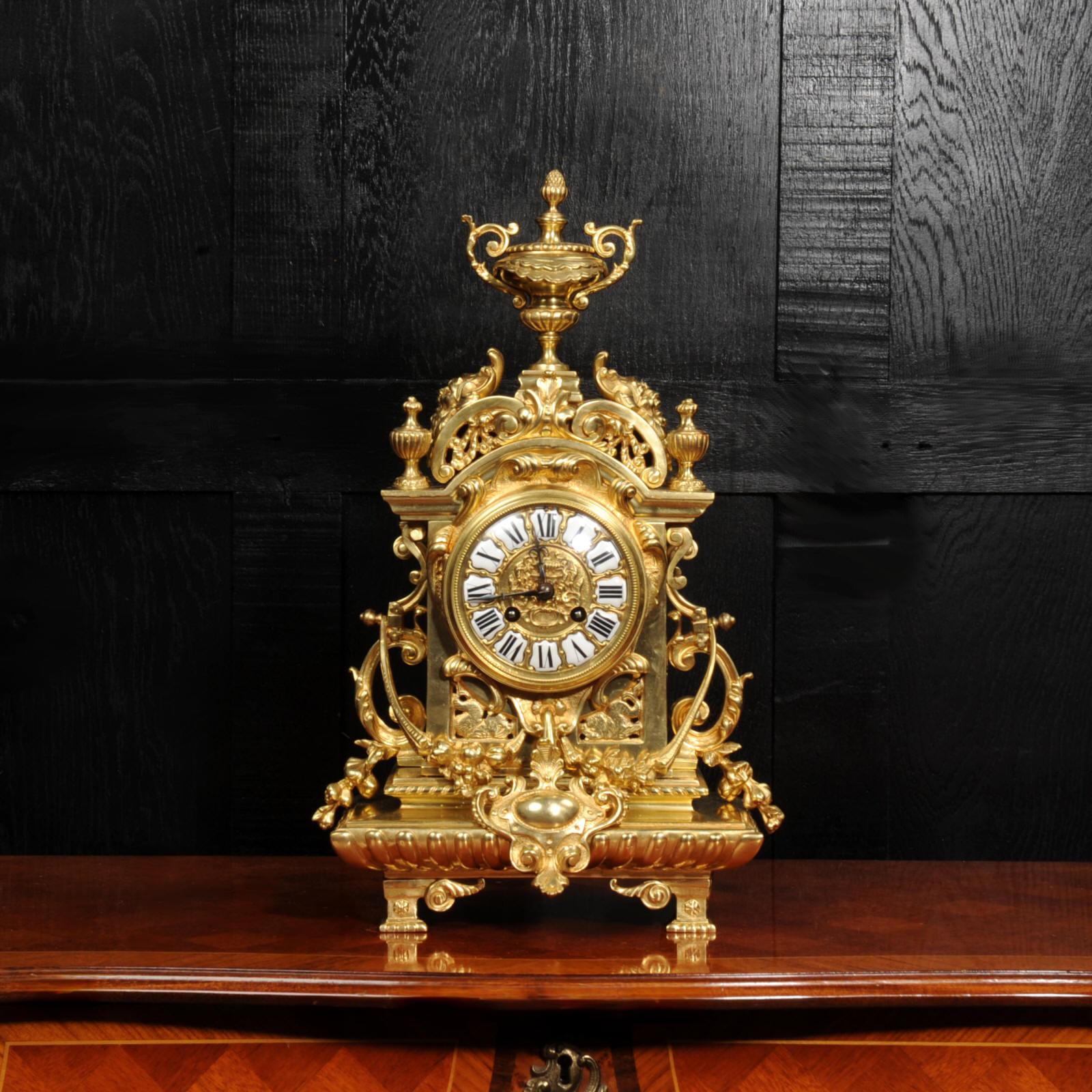 A large and stunning original antique French Baroque clock. Designed as a romantic ruin with an arched top with grotesque masks, fretted side panels and sitting on a gadrooned cushion base. To the sides are 'C' scrolls, and flowers and foliage are