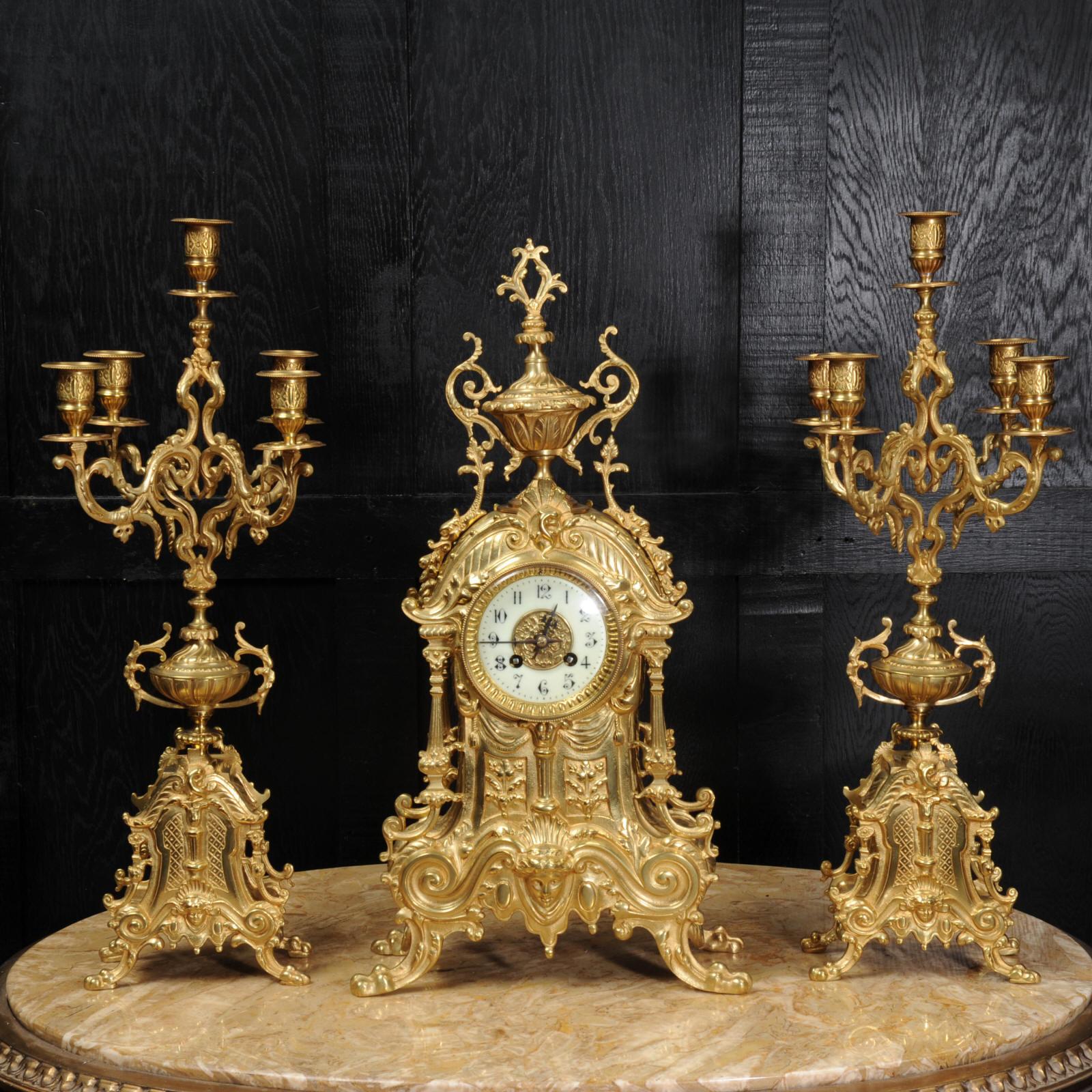 A beautiful original antique French clock set by Louis Japy. It is Baroque in style with bold scrolls, a goddess mask, acanthus urn and paw feet. Candelabra are conforming in style with five lights.

The dial is porcelain enamel on copper with