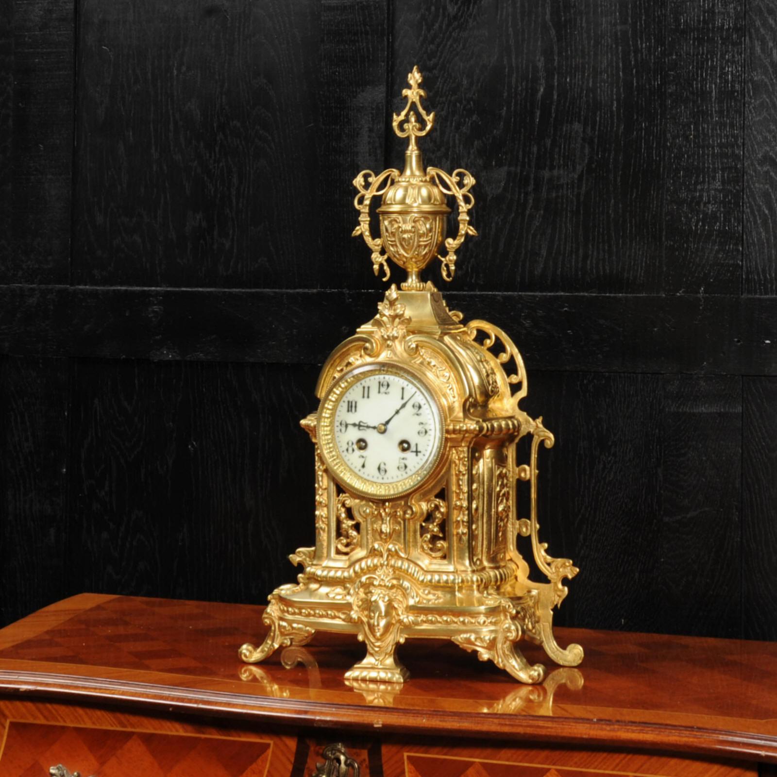 A lovely original antique French gilt bronze clock, beautifully modelled in the Baroque style and dating from around 1900. Decorated with scrolling acanthus, a goddess mask and a large, elaborate urn. The front is fretted to lighten the design and
