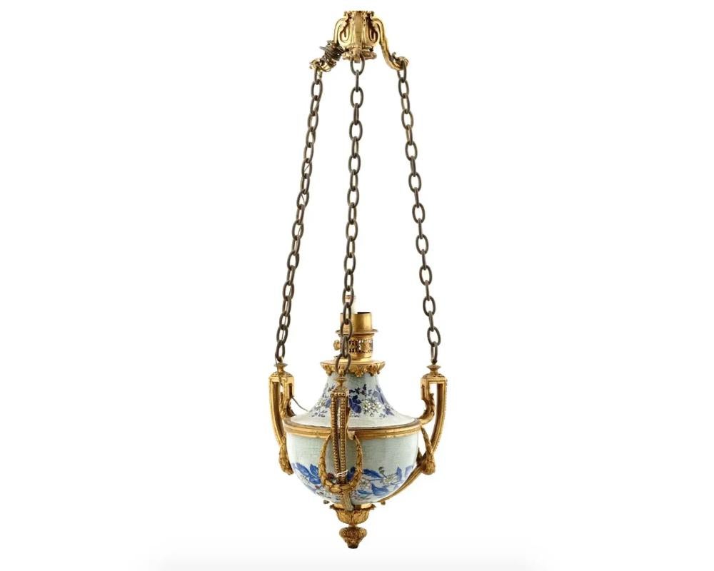 An antique late 19th-century French gilt bronze chandelier with modern electrical fittings. Crackle porcelain centerpiece with hand-painted flowers is hung on three chains. The bronze mounts have a Neoclassical garland motif. Hallmark Gagneau Freres