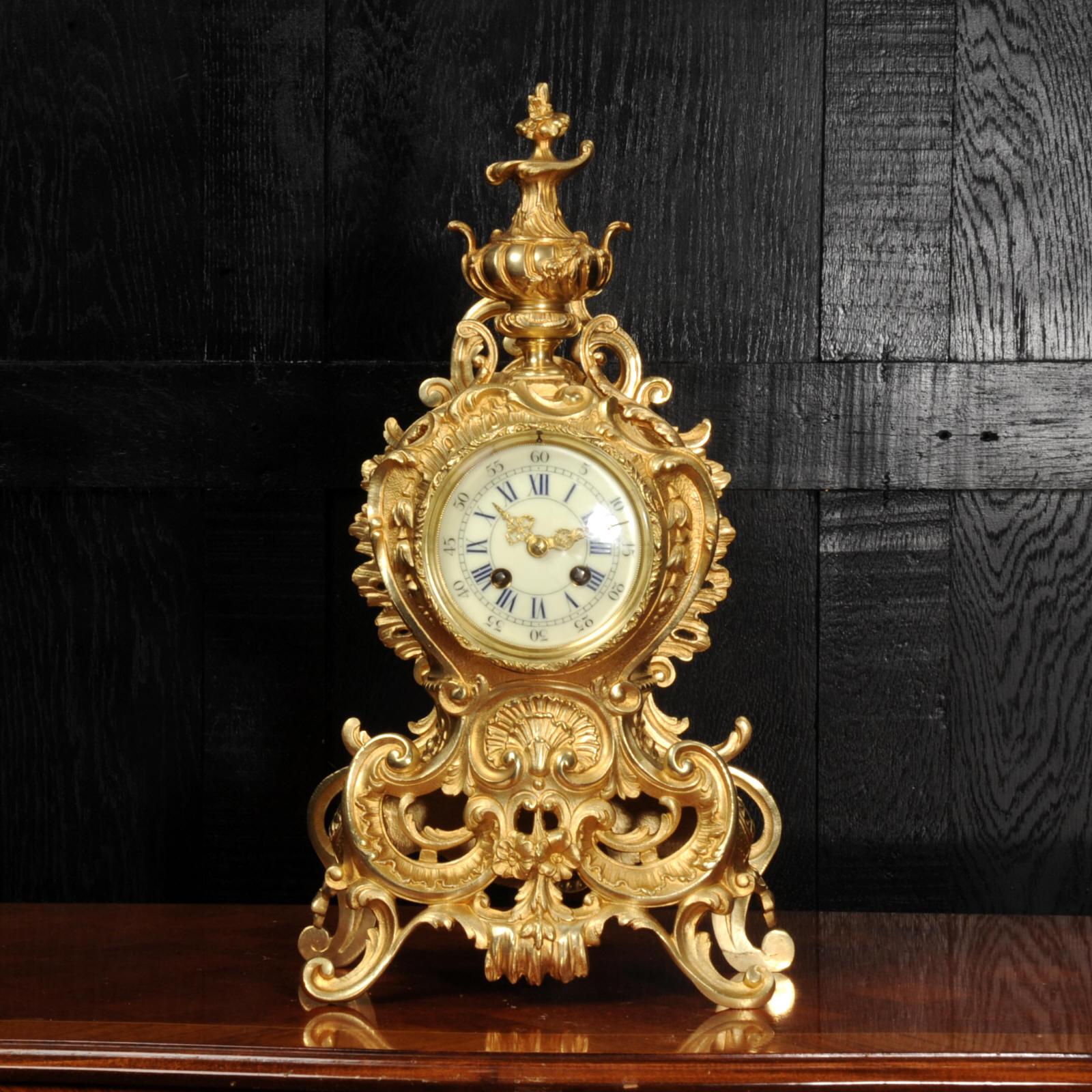 A stunning original antique French Rococo clock. It is beautifully modelled in gilded bronze, of waisted shape, profusely and boldly decorated with 'C' scrolls, acanthus leaves and trailing foliage. To the top is an elaborate urn. The front is