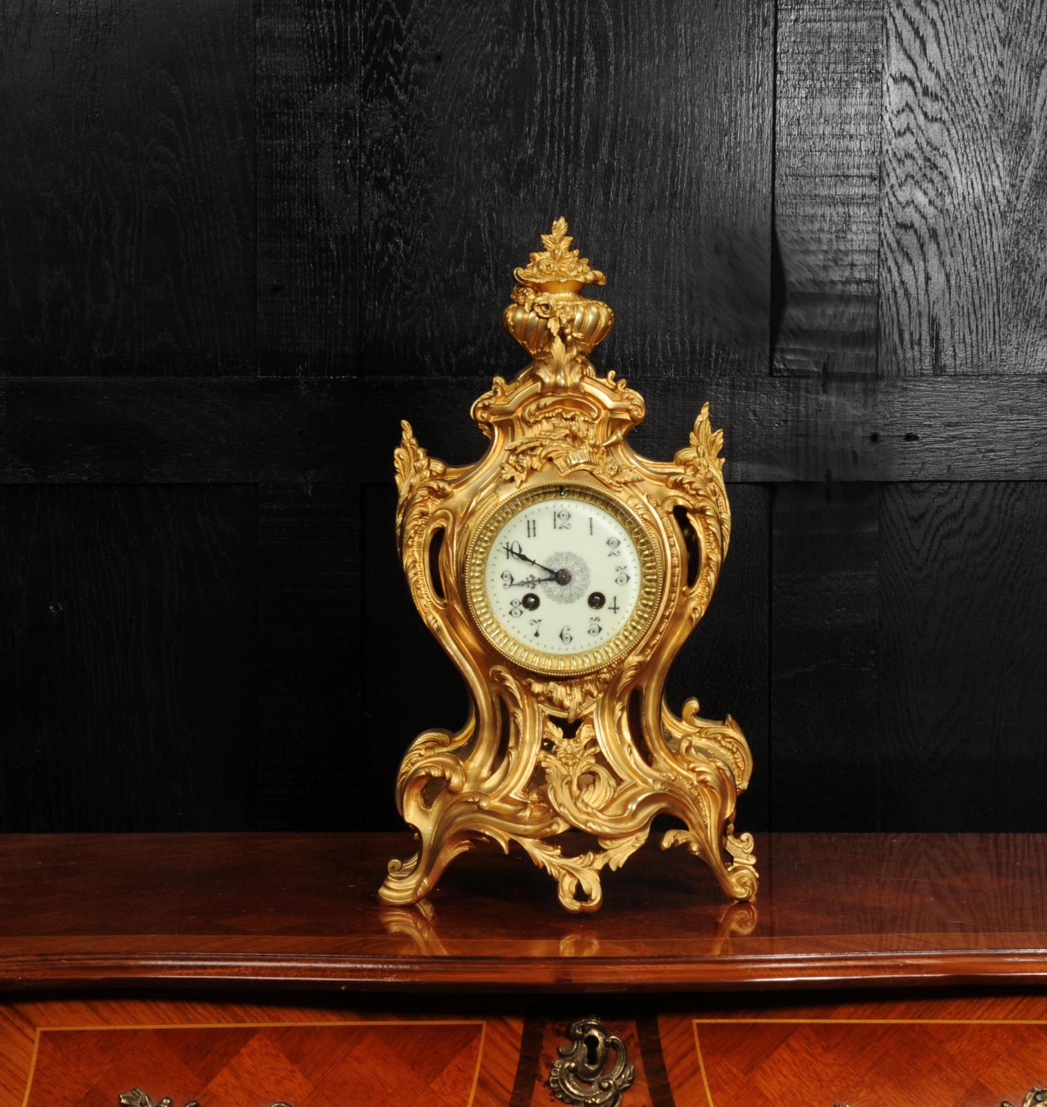A stunning original antique French gilt bronze clock by Samuel Marti. Beautifully made in he Rococo style, formed of sinuous curves of acanthus and scrolls, pieced to allow the pendulum to be glimpsed gently swinging within. Applied motifs and a