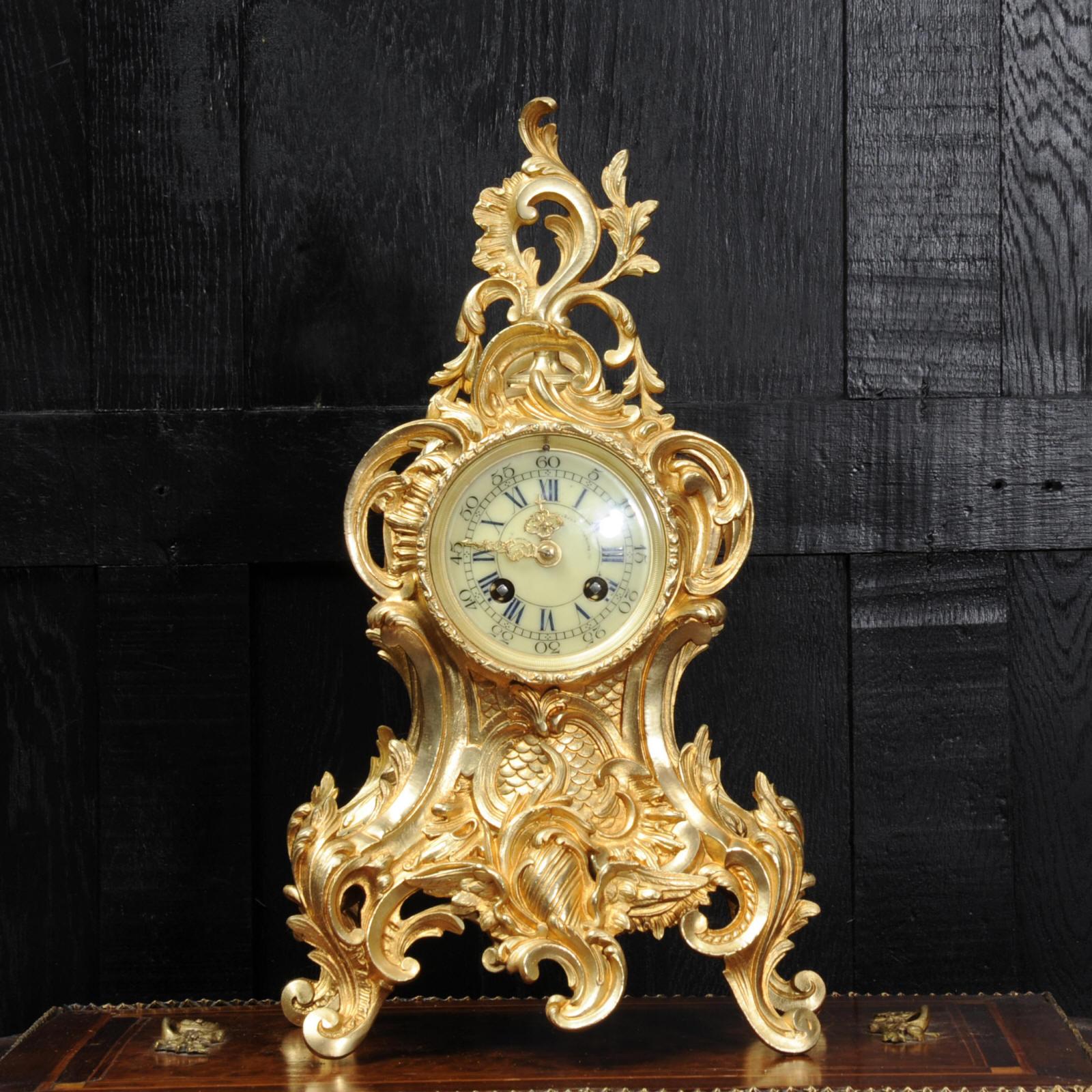 A lovely antique French clock by Louis Japy and retailed by Maison Henri Riondet of Paris, boldly modelled in the Rococo style in gilded bronze. Waisted keyhole shape profusely decorated with 'C' scrolls, and acanthus. To the top is an elaborate
