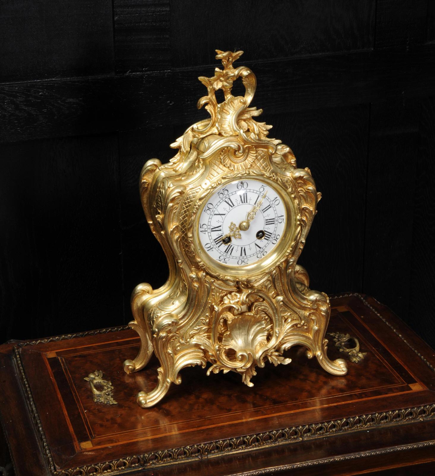 A lovely antique French clock, boldly modelled in the Rococo style in gilded bronze. Waisted keyhole shape profusely decorated with 'C' scrolls, and acanthus to the shoulders. A large shelf motif is mounted to the front and to the top is an