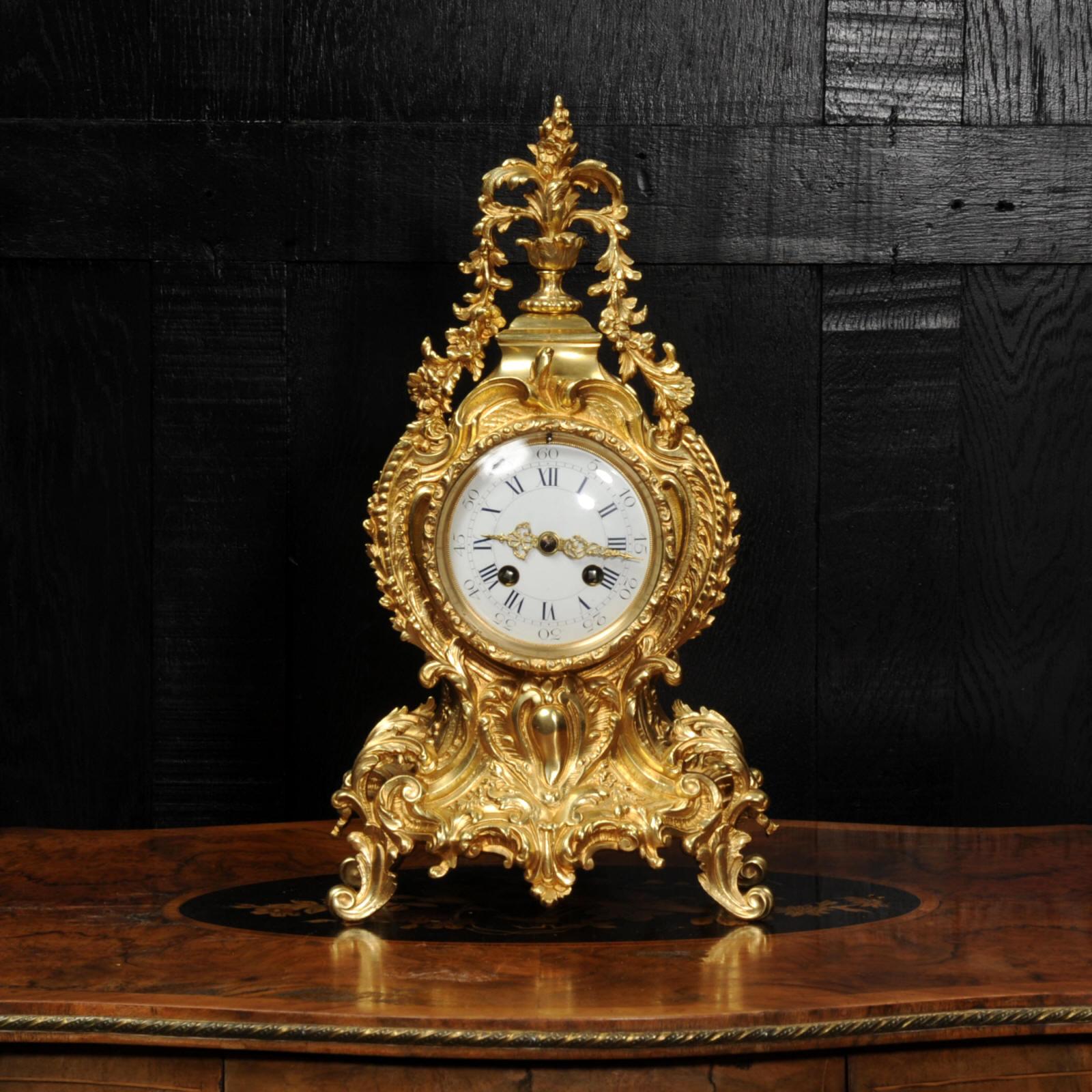 A stunning original antique French Rococo clock. Beautifully made in gilded bronze, waisted case decorated with 'c' scrolls, acanthus leaves and abundant floral swags tumbling from the leafy finial.

The large dial is porcelain enamel on copper