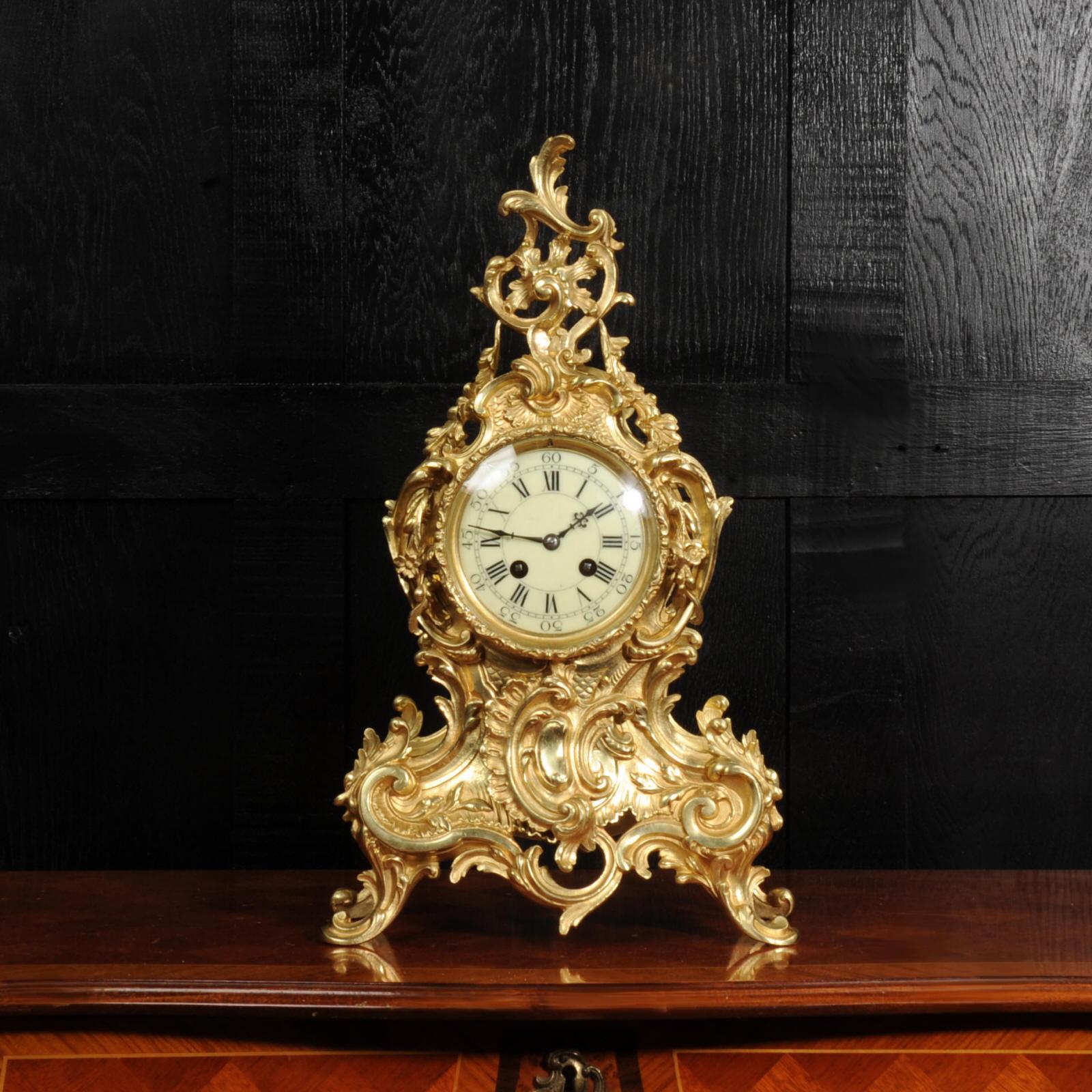 A stunning and large original antique French gilded bronze clock. It is of the most beautiful Rococo style, waisted case decorated with 'C' scrolls, acanthus leaves and floral swags. To the top is a Rococo flourish with trailing floral swags.

The