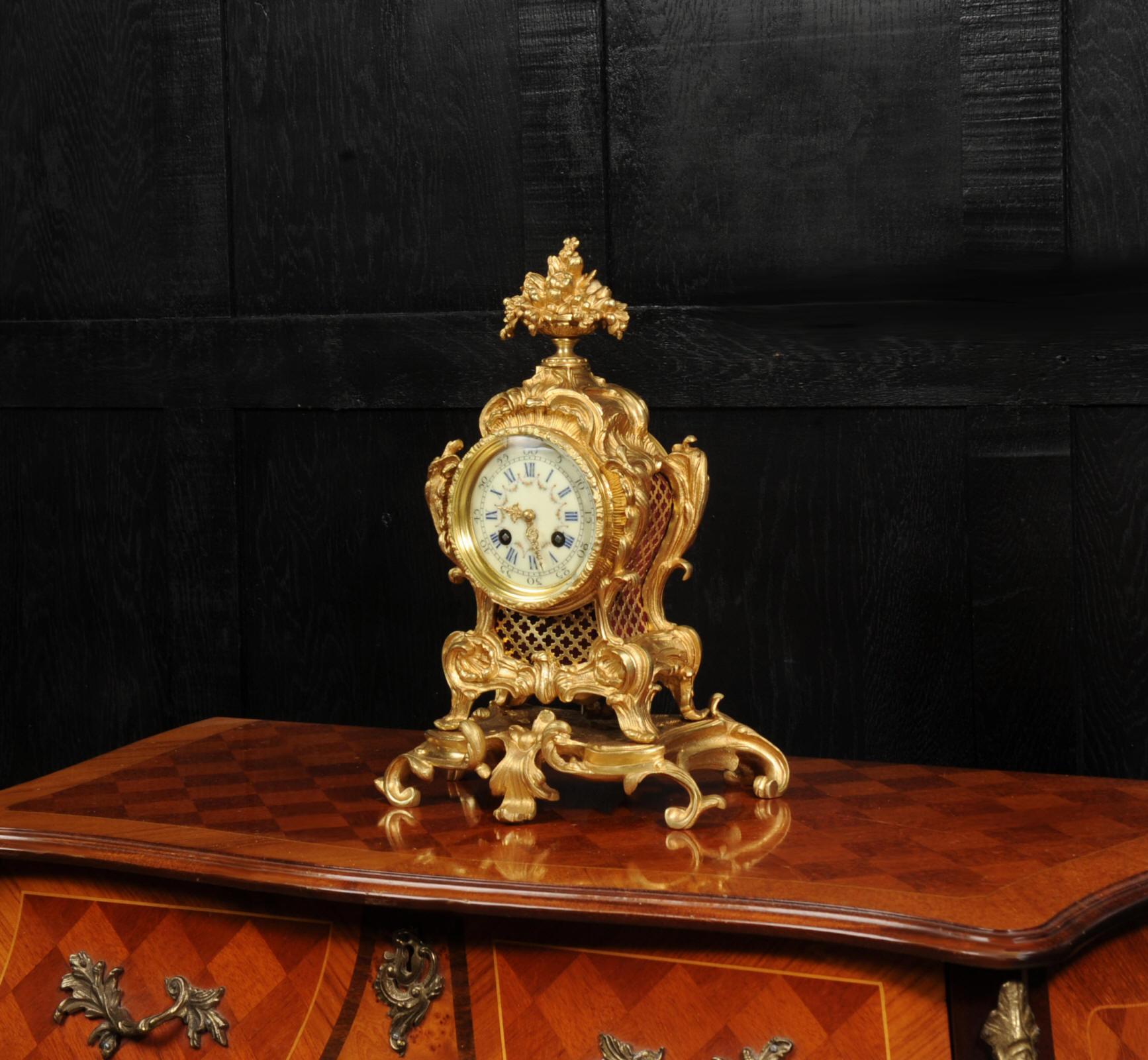 A beautiful clock of ornate Rococo design, the case finely cast with scrolling acanthus and rocaille ornament, the front and sides with pierced lattice panels back with fabric, raised upon a shaped plinth with boldly scrolling feet. The circular