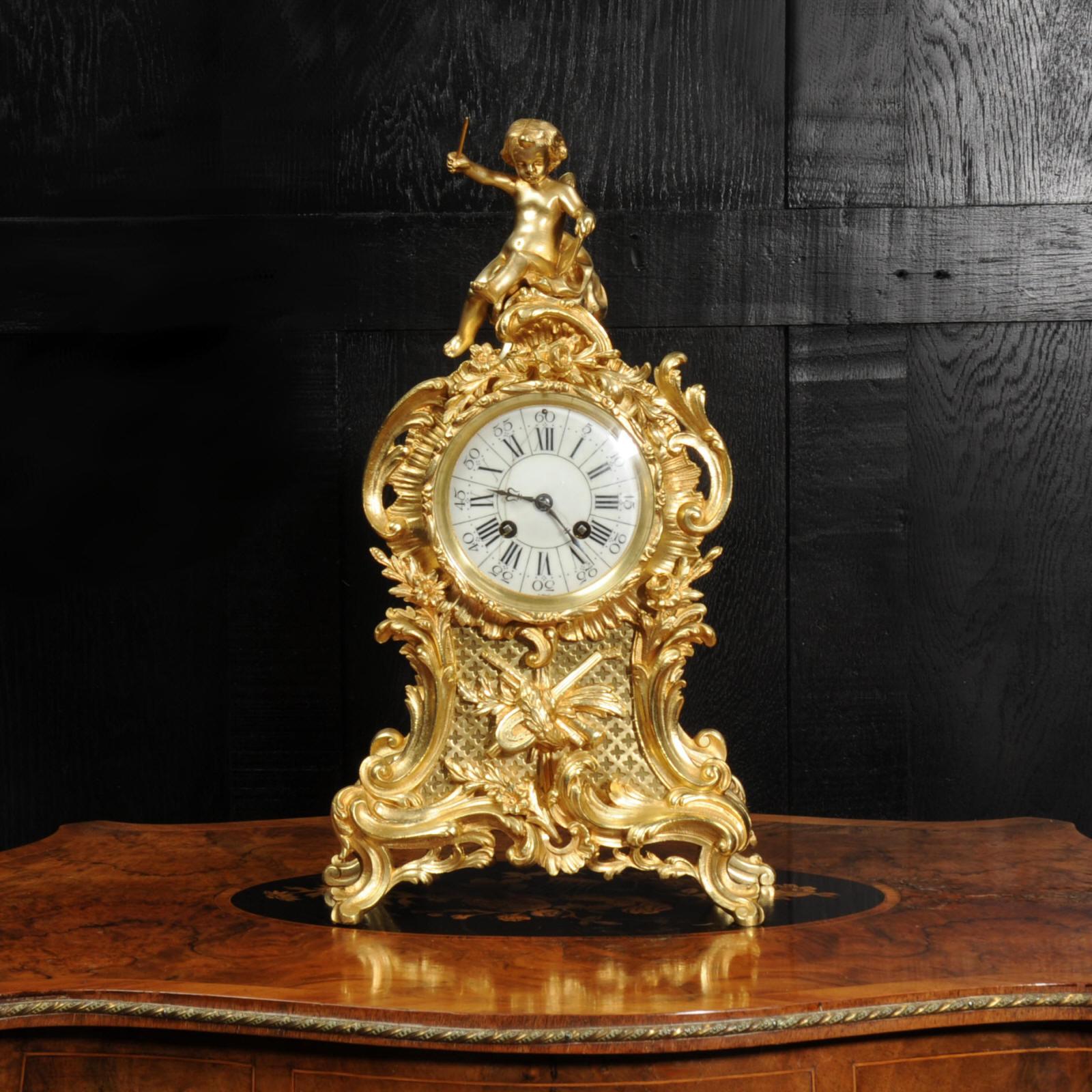 A lovely original antique French Rococo clock by Vincenti et Cie. Flamboyantly modelled in gilded bronze, waisted case with with swirling acanthus, 'c' scrolls and floral swags. To the front is a panel of fret work with a motif of musical