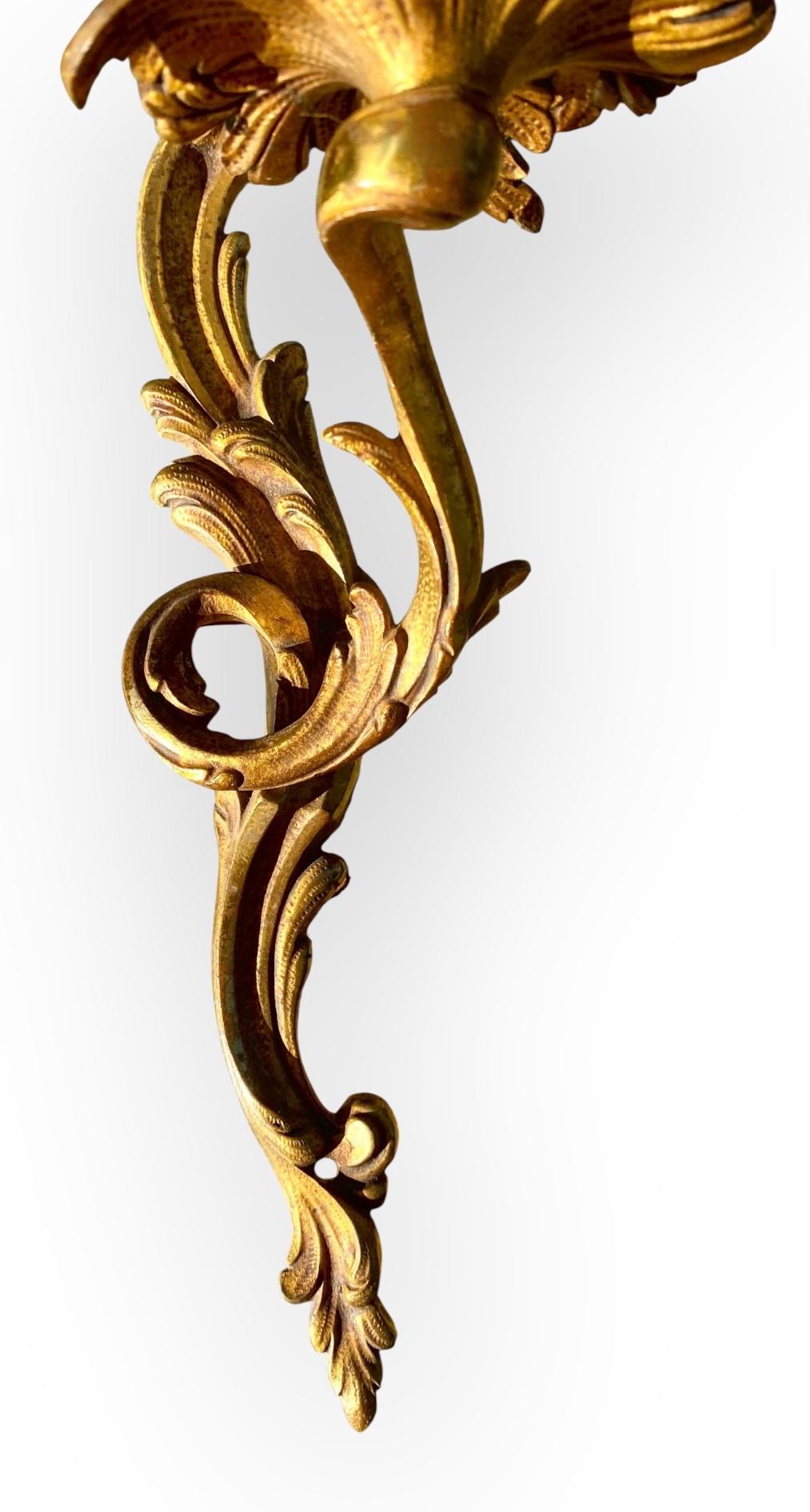 Aplique de pared antiguo francés, de bronce dorado, con ornamentación de hojas de acanto y pantalla de tela.

Presenta elementos decorativos intrincados, como roleos y motivos foliados, típicos de estilos como Luis XV o Luis XVI.
Presenta una única