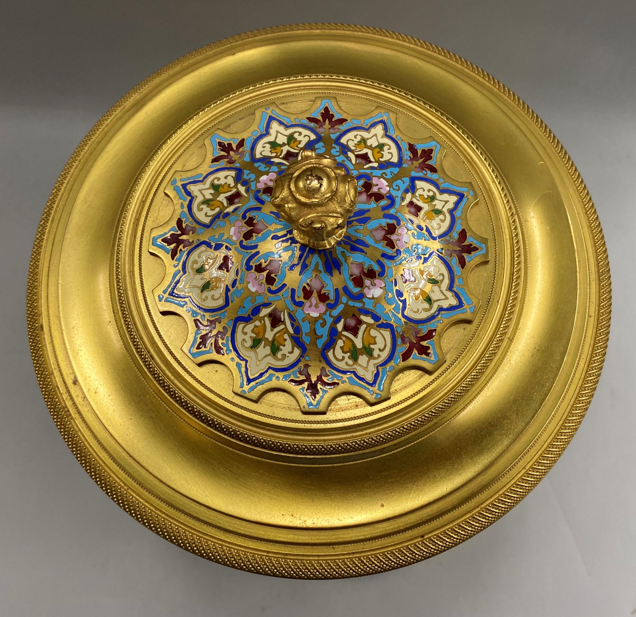 A beautiful gilt champlevé mantel clock with a 4.5 inch champlevé bordered porcelain dial with bold Arabic numerals, four beveled glass curved panels, two of which are access doors on the front and back, original champlevé pendulum, and brass 8 day