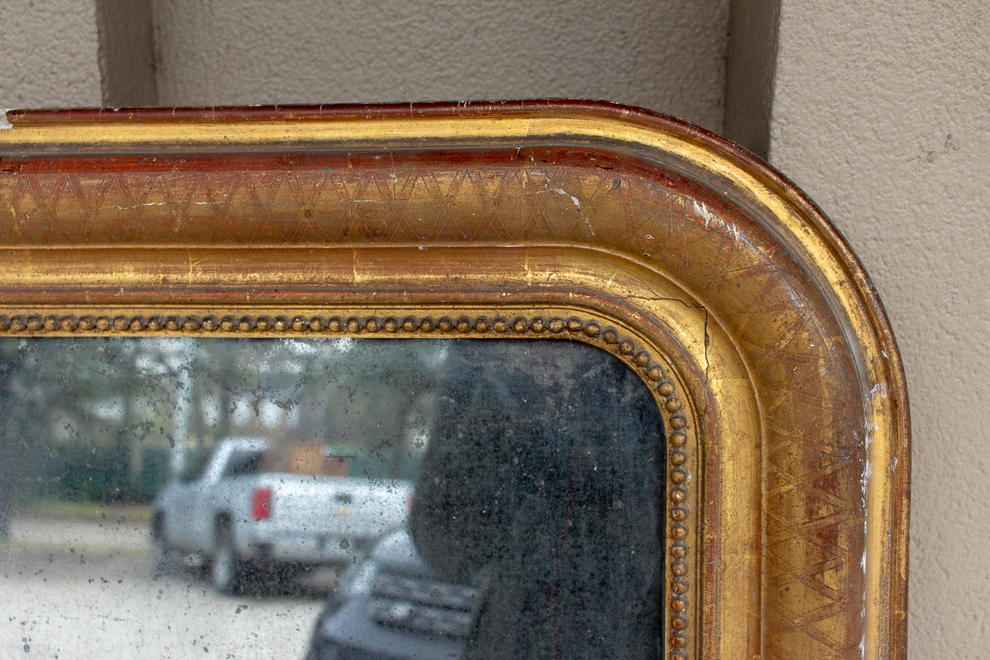 This antique French Louis Philippe mirror features a very distressed frame and storm-cloud gray glass. The age in this mirror is quite stunning. There are defects to the frame and areas where the gilt has been damaged or chipped. Please see all