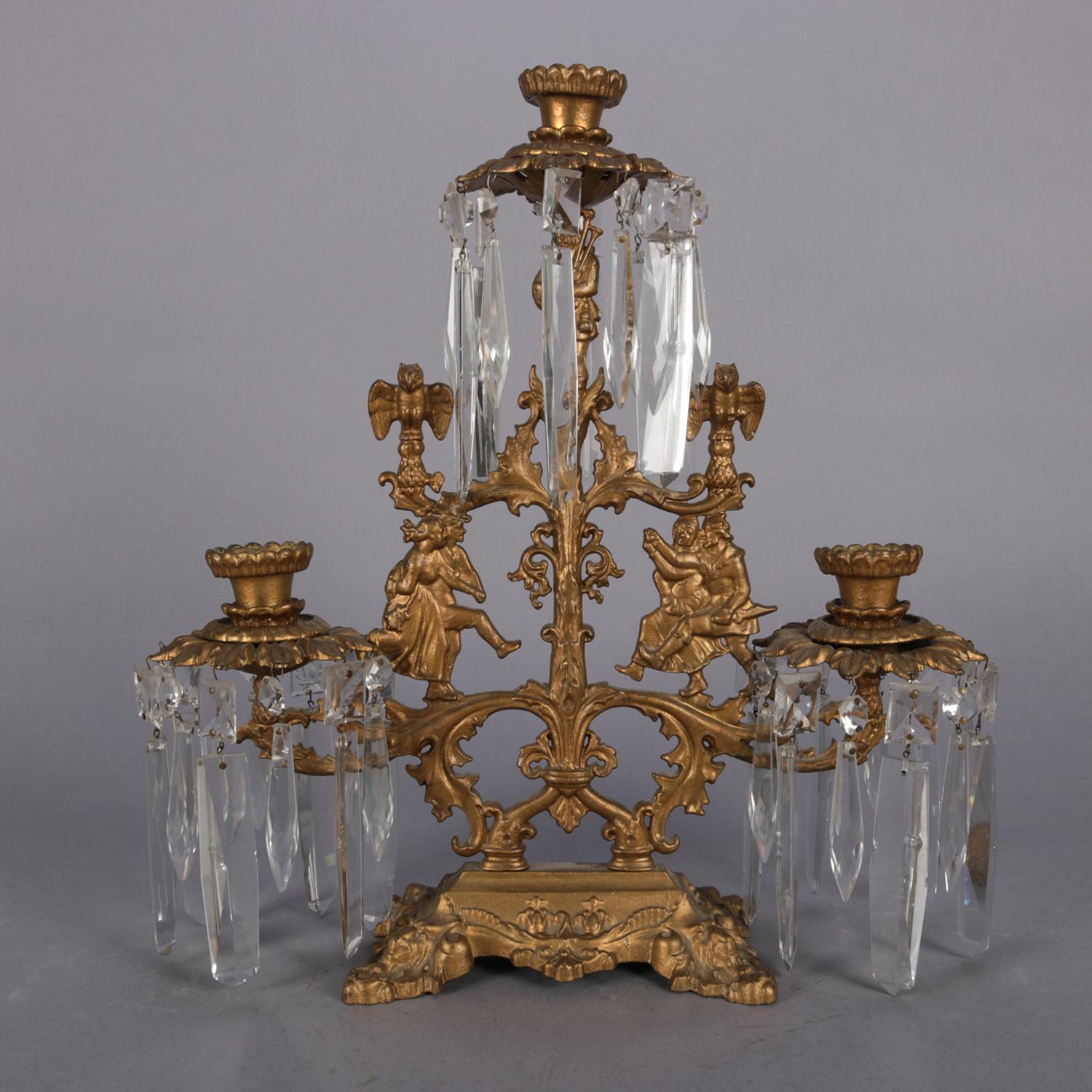 Antique French girandole candelabra features gilt cast metal construction with courting couples and foliate decoration over footed base and having three candle sockets with hanging cut crystals throughout, circa 1890.

Measures:17