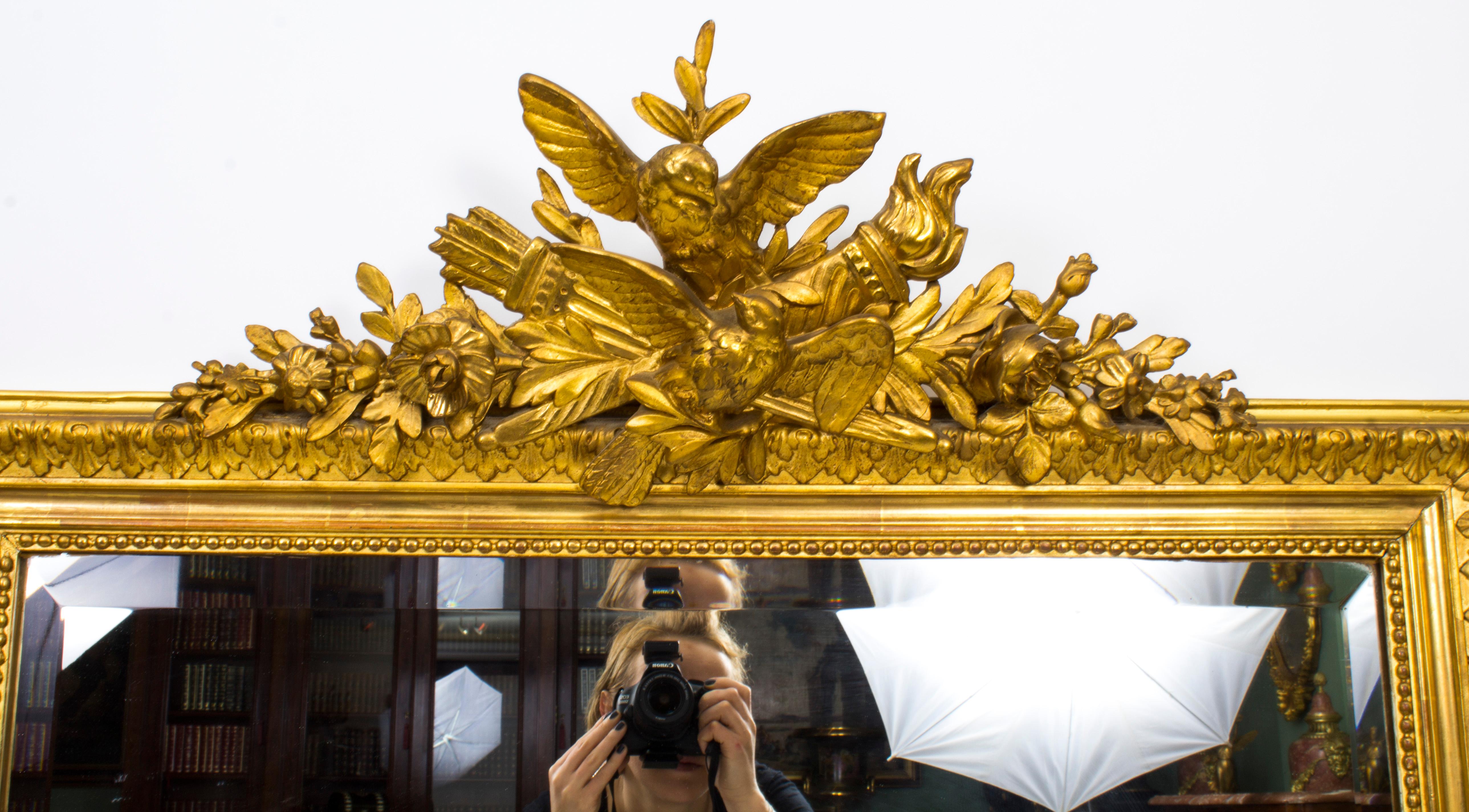 This is a beautiful large antique French carved giltwood overmantel mirror, C 1860 in date.
The frame is surmounted with a striking carved giltwood central finial with doves, a flaming torch, a quiver of arrows and foliate and floral decoration.