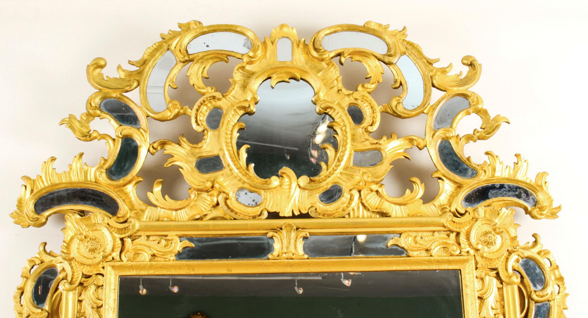 This is a spectacular antique French Rococo giltwood overmantle mirror, circa 1780 in date.

The shaped symmetrical frame with central mirror plate that is framed with marginal side plates. It is a profusely carved giltwood frame decorated with C