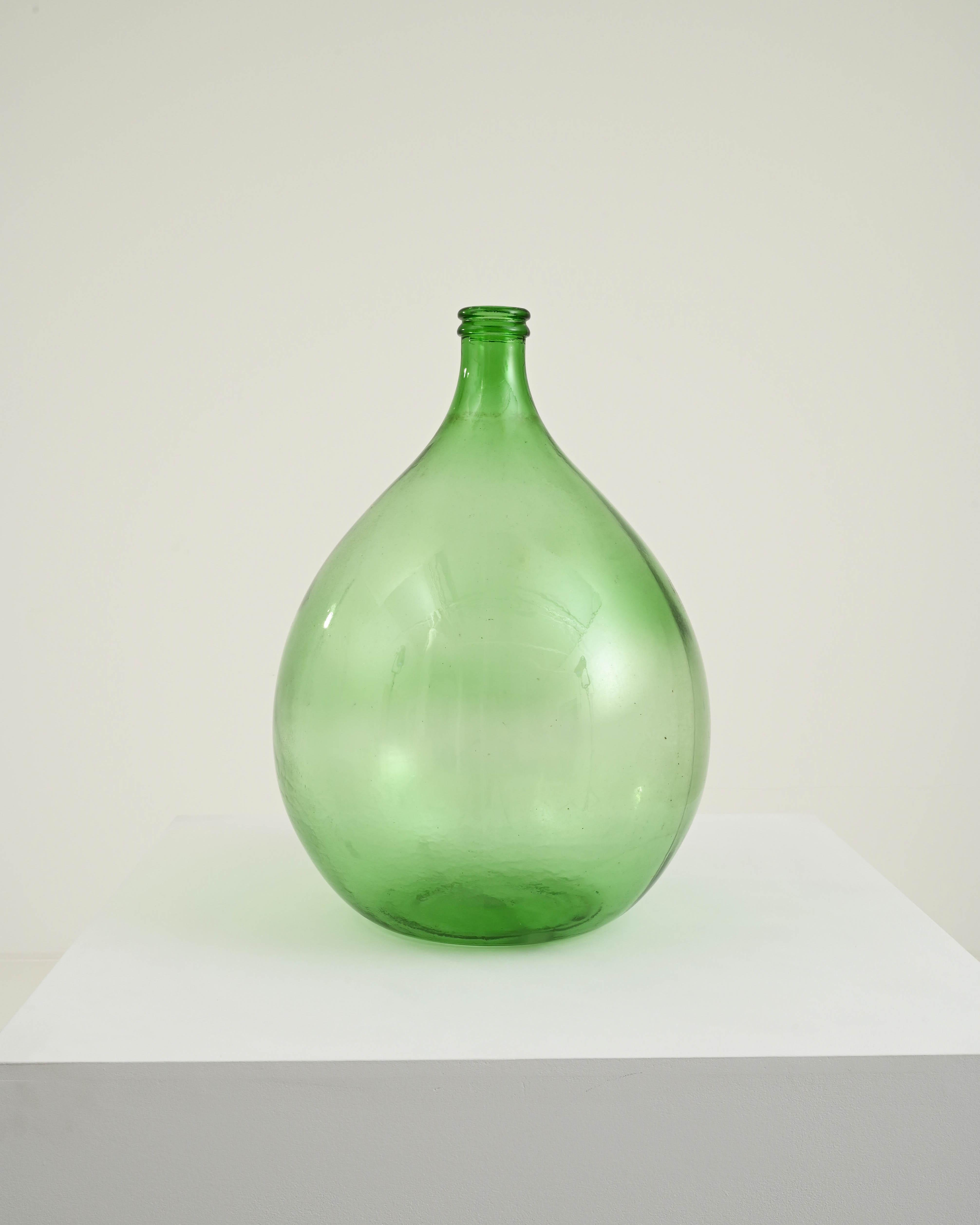 Also called a ‘demijohn’ or ‘carboy’ this glass vessel was made in France around 1900 for the purpose of fermenting, conditioning or transporting alcoholic beverages. A slender bottleneck blooms out into a broad globe shape; the absinthe-green tone