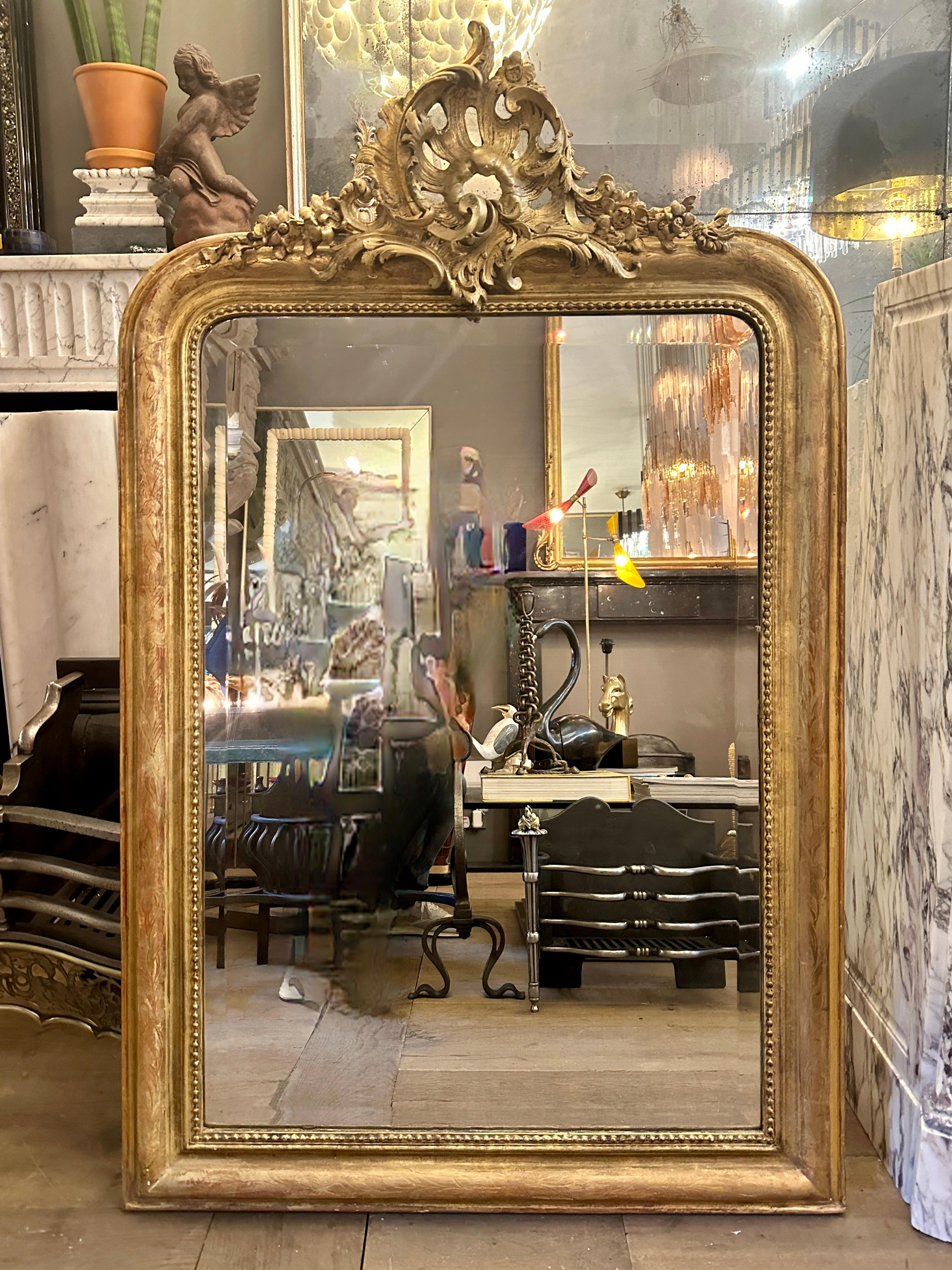 An antique mid 19th century French Rococo style gold gilt crested mirror.
The original bevelled plate still intact and relatively fox free. The frame with warm worn gilt work and beaded inner slip. The large Rococo asymmetrical cartouche nearly