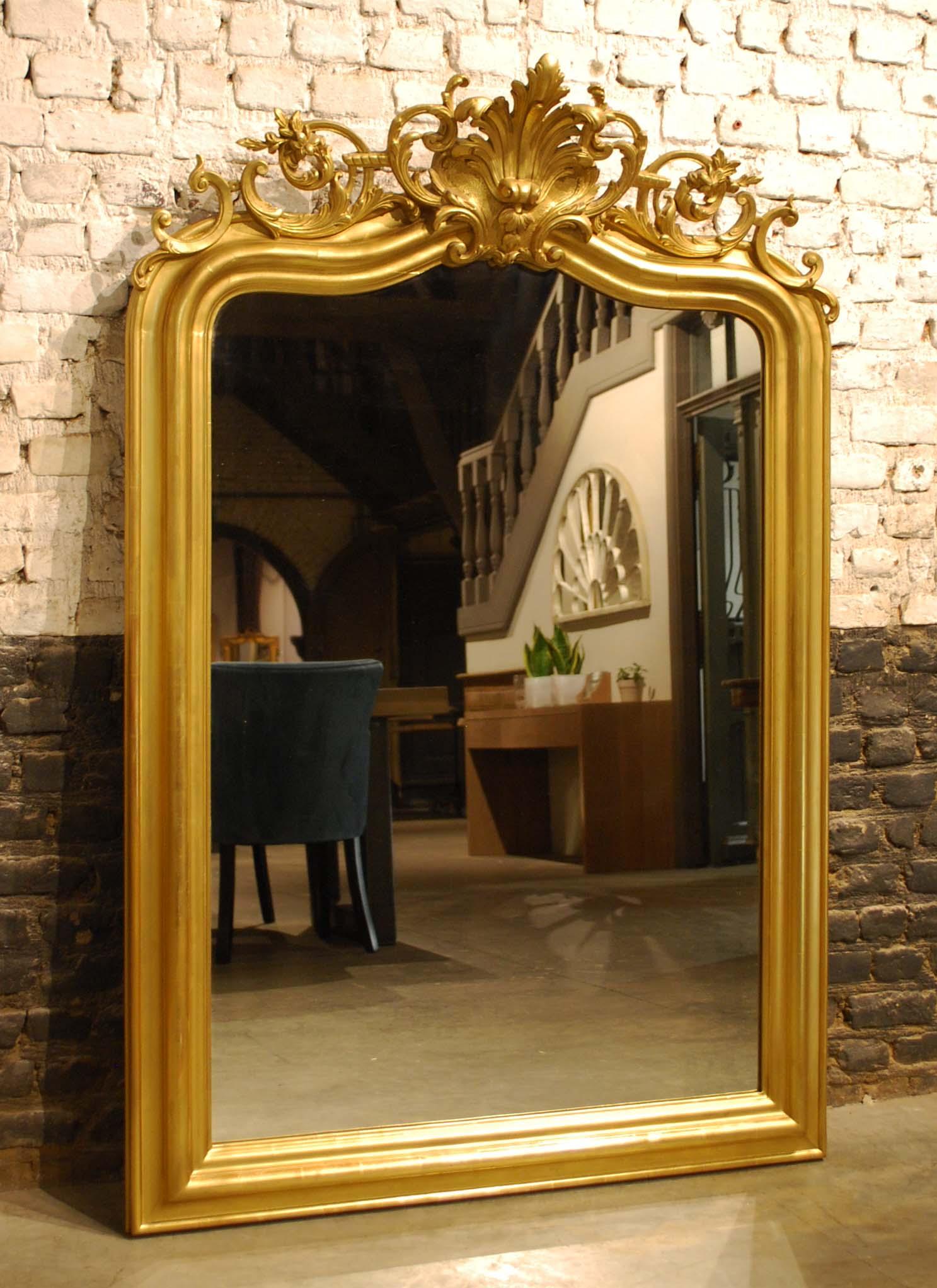 This beautiful antique Louis Philippe mirror was made in Southern France and dates circa 1850.
The frame is partly gold leaf gilt and partly gilded with gold paint. The sculpted cartouche or crest on top is centered upon two stylized acanthi