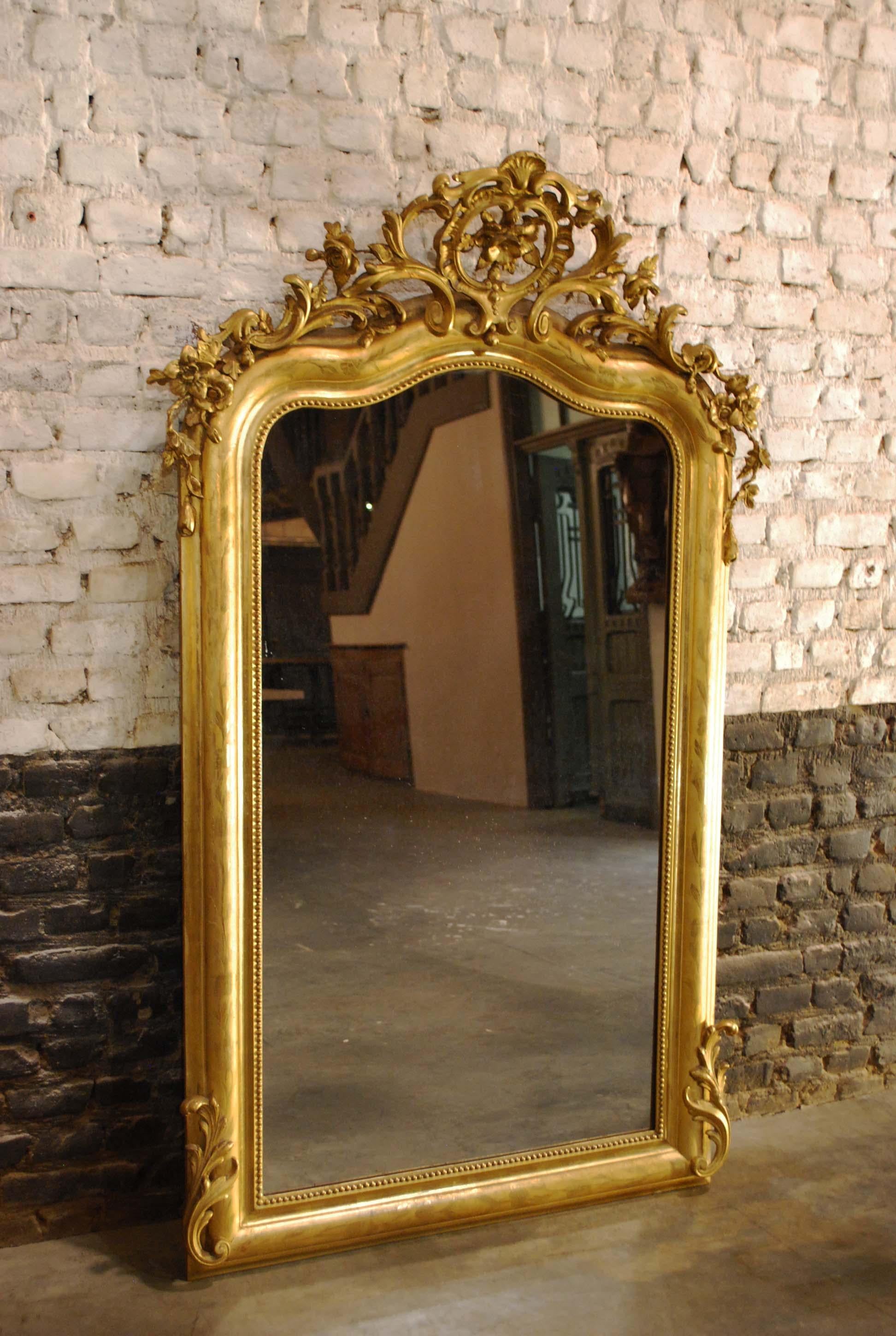 This beautiful antique Louis Philippe mirror was made in Southern France and dates approximately 1850. 
The frame is completely gold leaf gilt and is adorned with wonderful ornaments. The sculpted cartouche or crest on top is centered upon two c