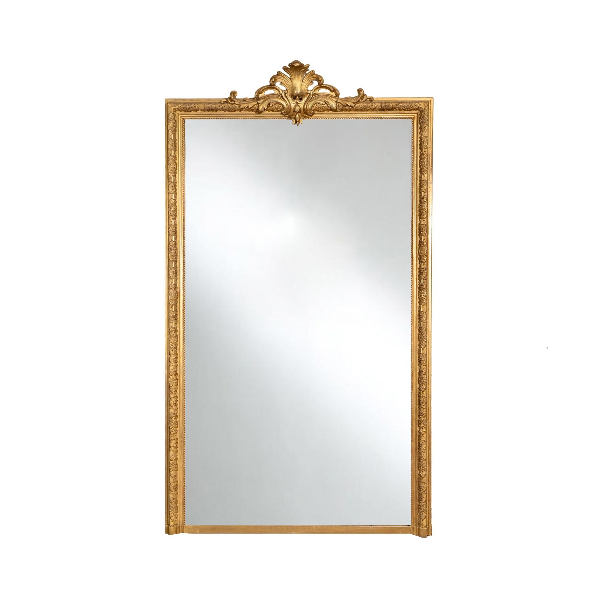 Miroir français ancien du XIXe siècle, doté d'un cadre en bois sculpté à la main et orné d'une élégante finition à la feuille d'or. Le cadre présente des détails décoratifs complexes, couronnés par un arc de style rococo au sommet, ce qui ajoute une