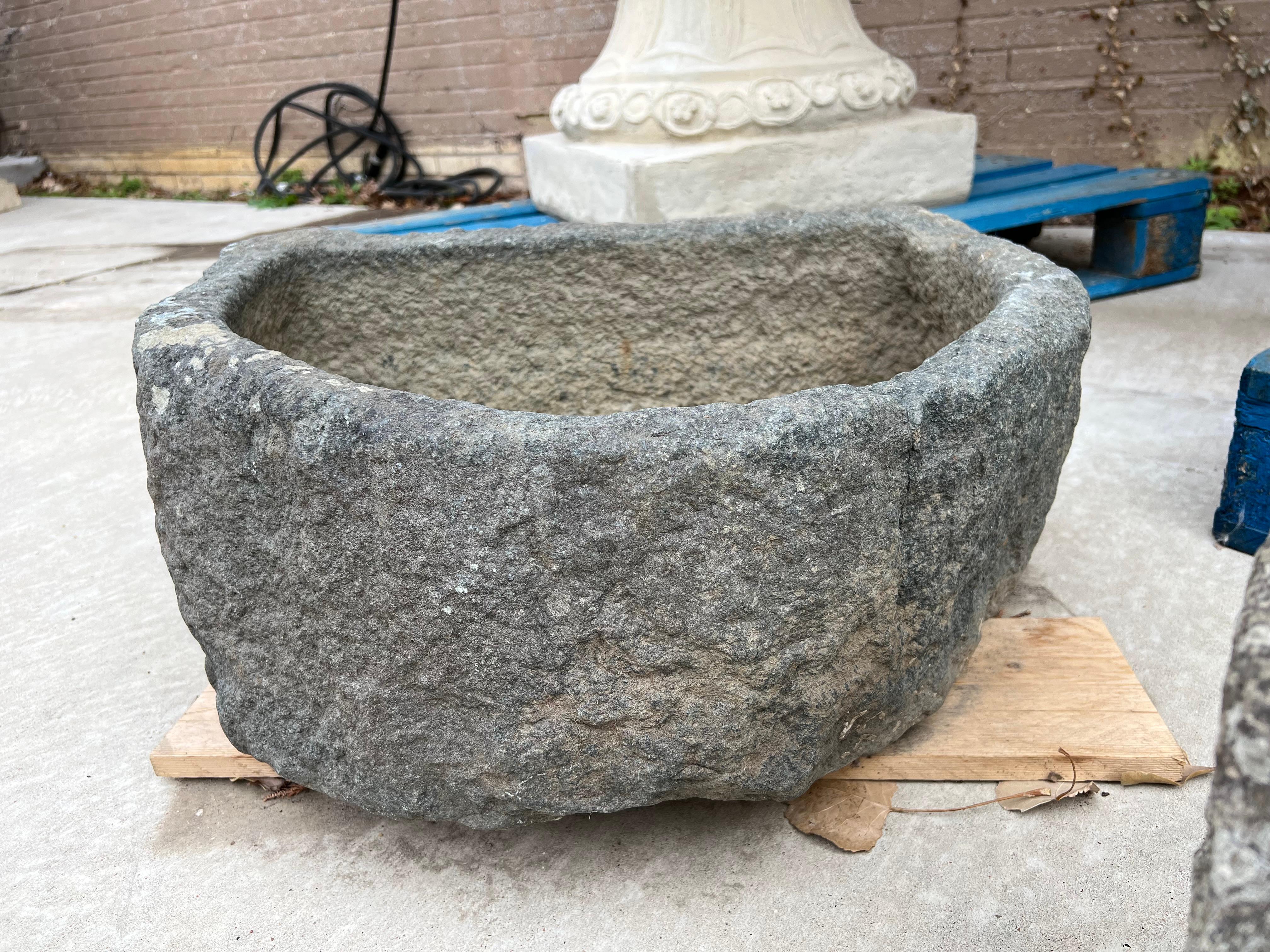 This robust demi-lune trough was hand carved in Normandy, France, in the 1800s. The stone used was a local granite, which is difficult to work with due to its hardness. Dark gray in color, with a natural dotted beige, white, and brown patina, the