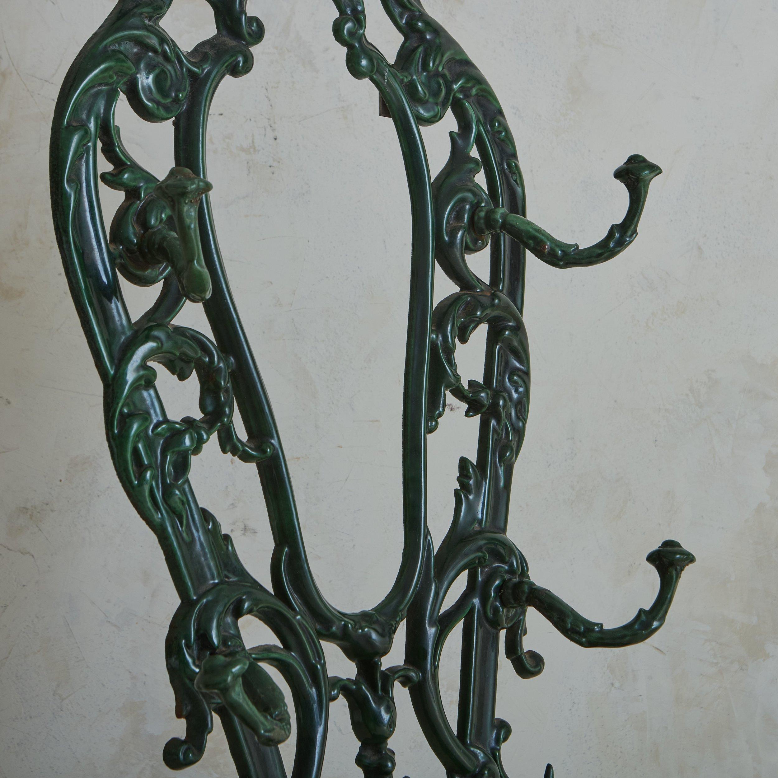 A free standing antique French cast iron coat rack or hallway tree featuring an intricate frame with curl and scroll motifs. This piece was painted a vibrant green hue; it has a demilune table top and six hooks for hanging coats or hats. The lower