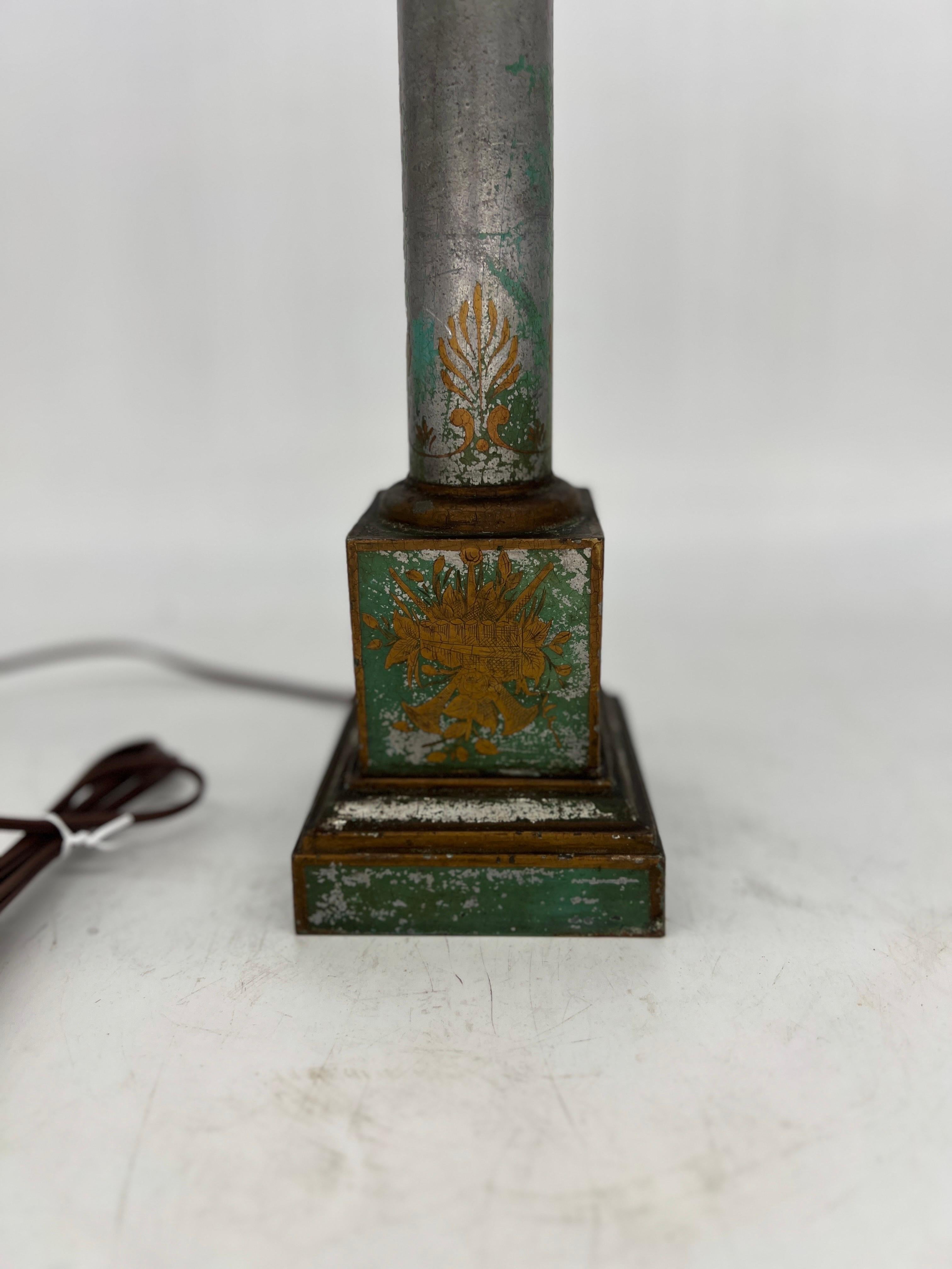 French, early 20th century. 

An antique neoclassical style table lamp. The lamp features a traditional column model form with a silver tole base which has original green paint to surface and accented by gilt lyre, botanical and other motifs.