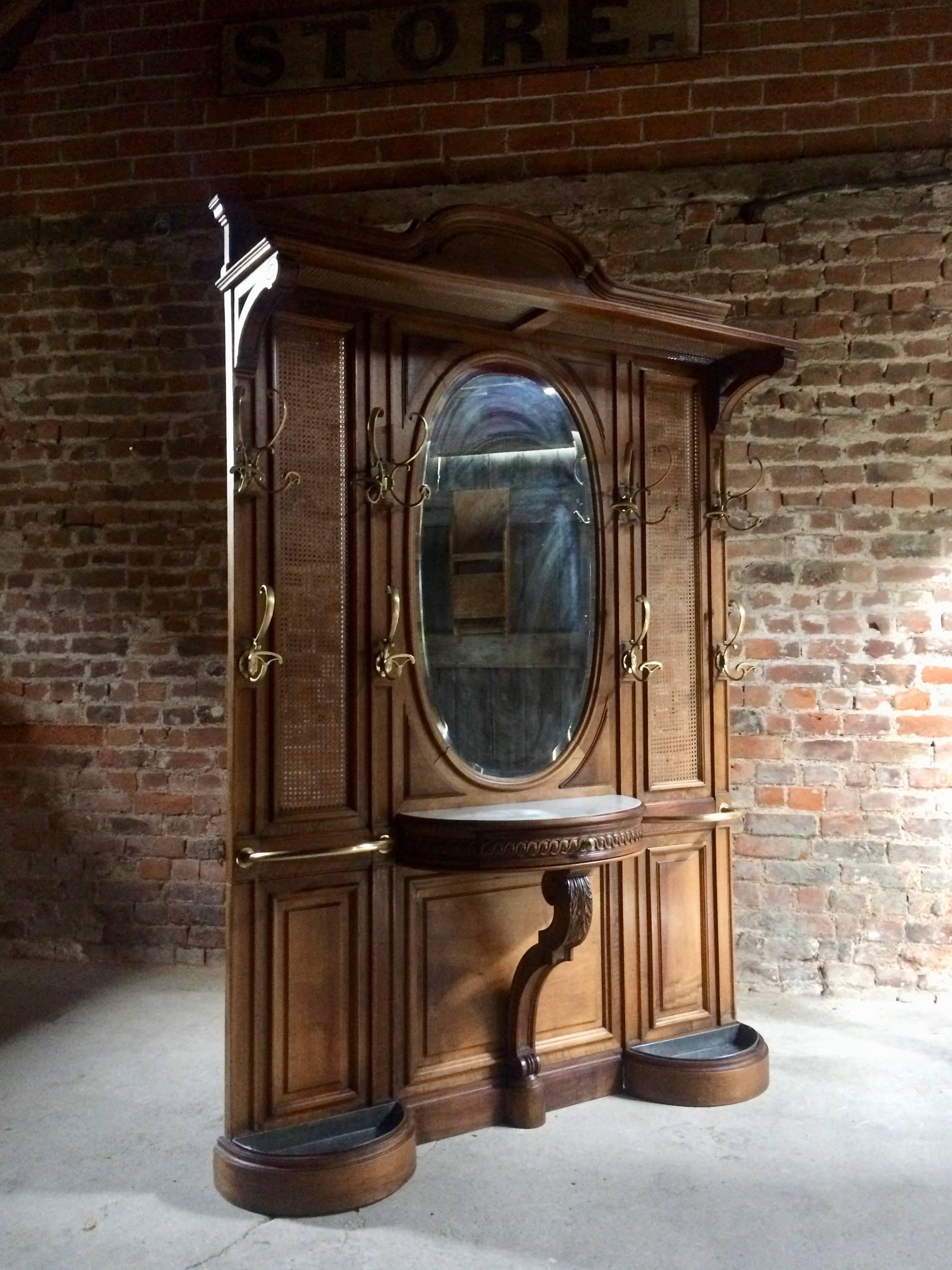 A magnificent large and imposing late 19th century French chateau walnut and bergere caned hall stand, circa 1890, with central bevelled oval mirror flanked by twelve brass hooks, over a demi-lune marble top glove drawer console and twin drip trays