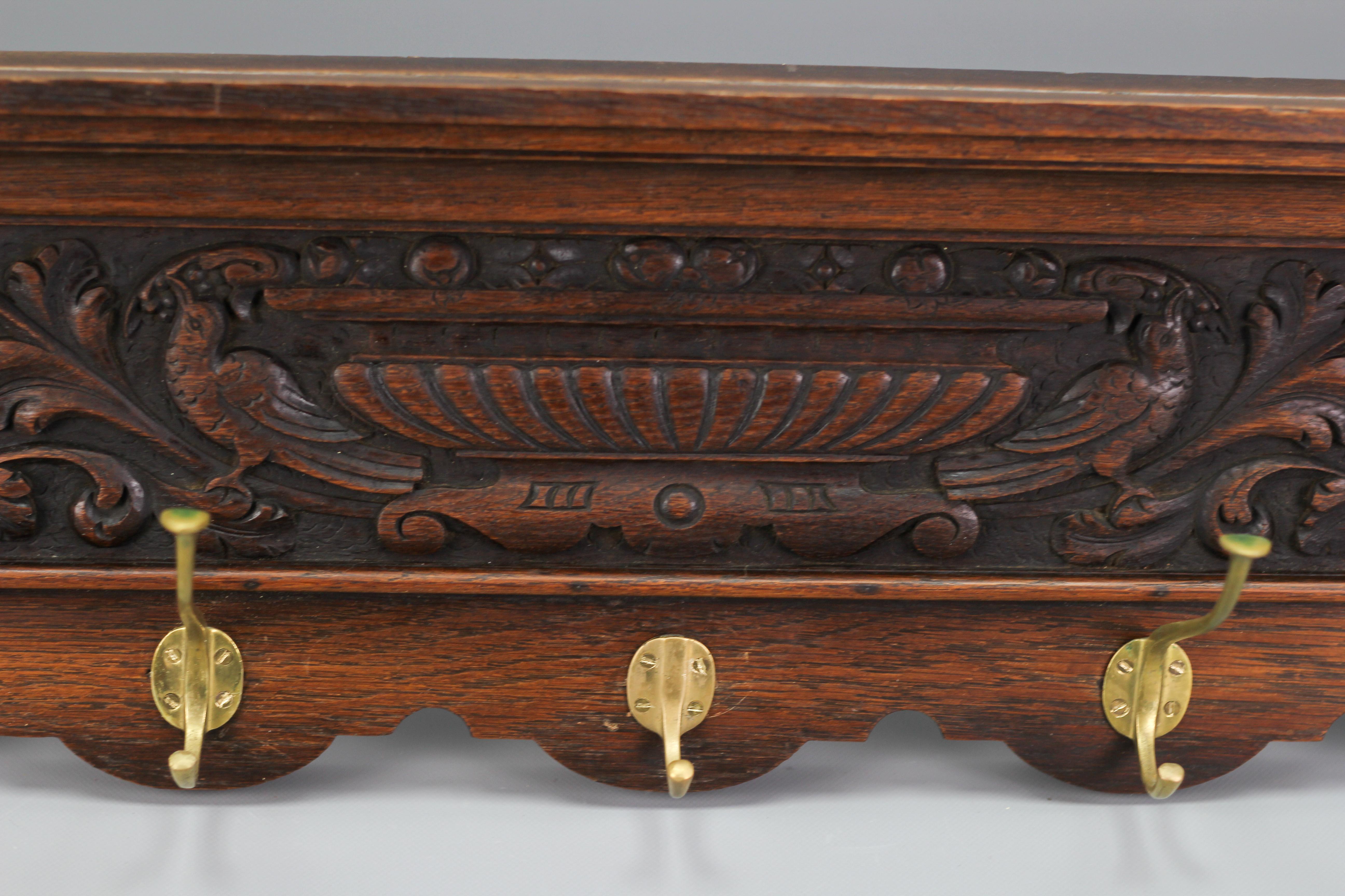 Impressive French hand-carved solid oak wall hanging coat rack from the early 20th century. This beautiful coat rack or hall shelf features stunning carvings of two lion heads at each end of the shelf, adorned with scrolled leaves and birds in the