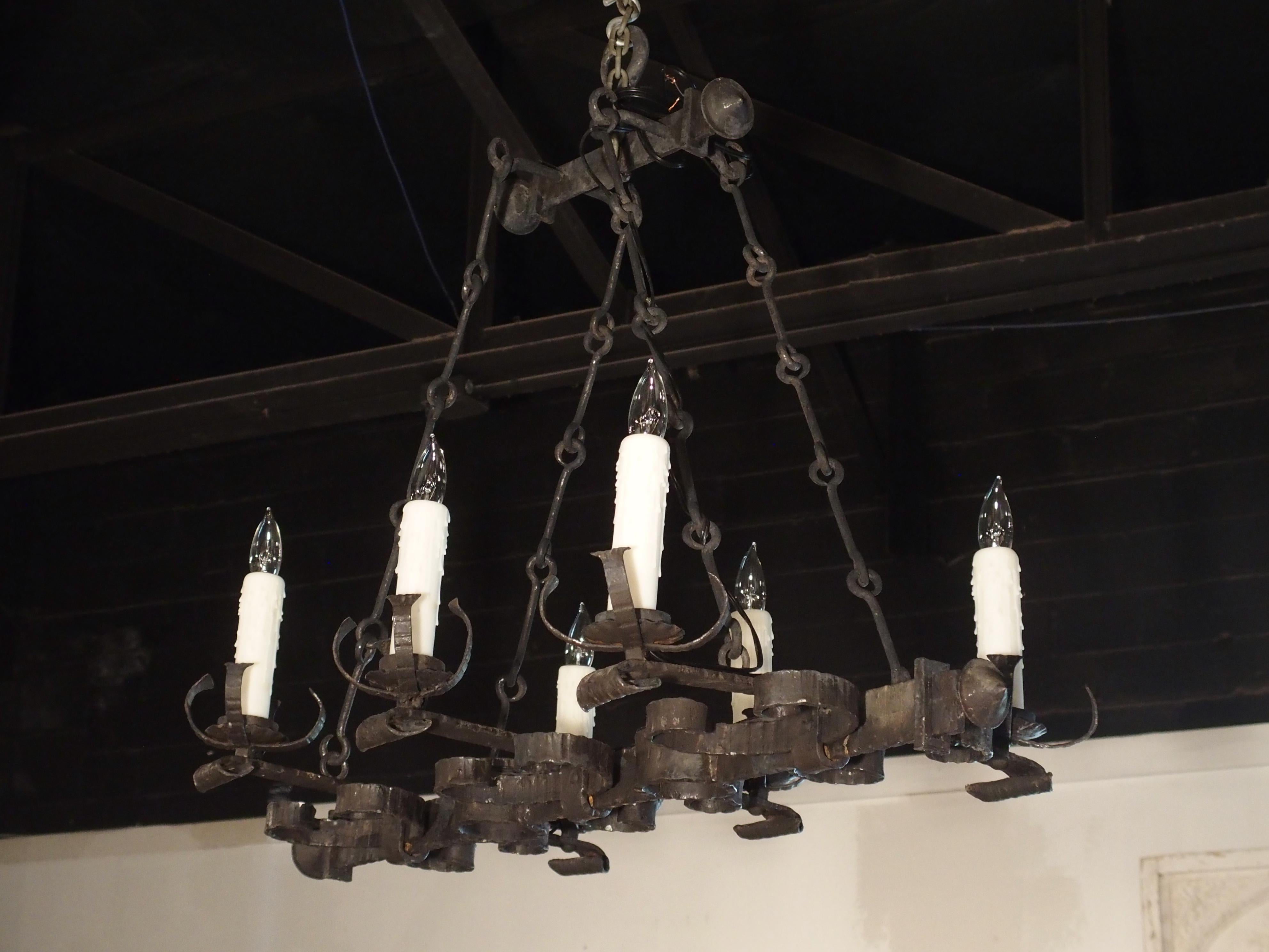 This antique, rectangular French iron chandelier has a myriad of interesting hand forged shapes made from thick iron ornamentation. There are linear ridges hammered into the iron bars which are offset by circular motifs. There are C-scroll motifs,