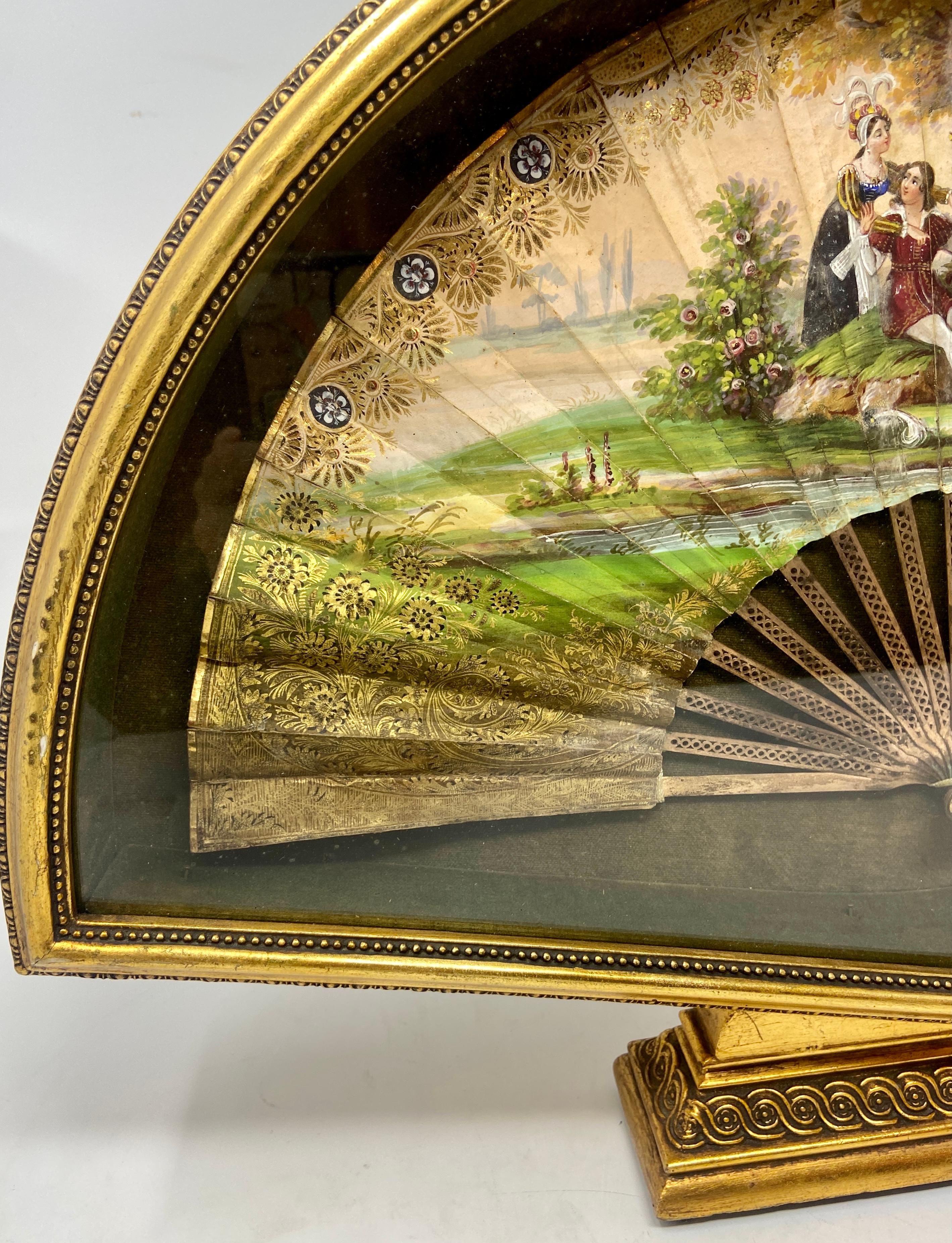 Antique French fine hand-painted fan with gold bronze guards in a giltwood shadow box, circa 1850s. Beautifully painted pastoral scene on the fan, which is placed in an intricately carved and wonderful old shadowbox.