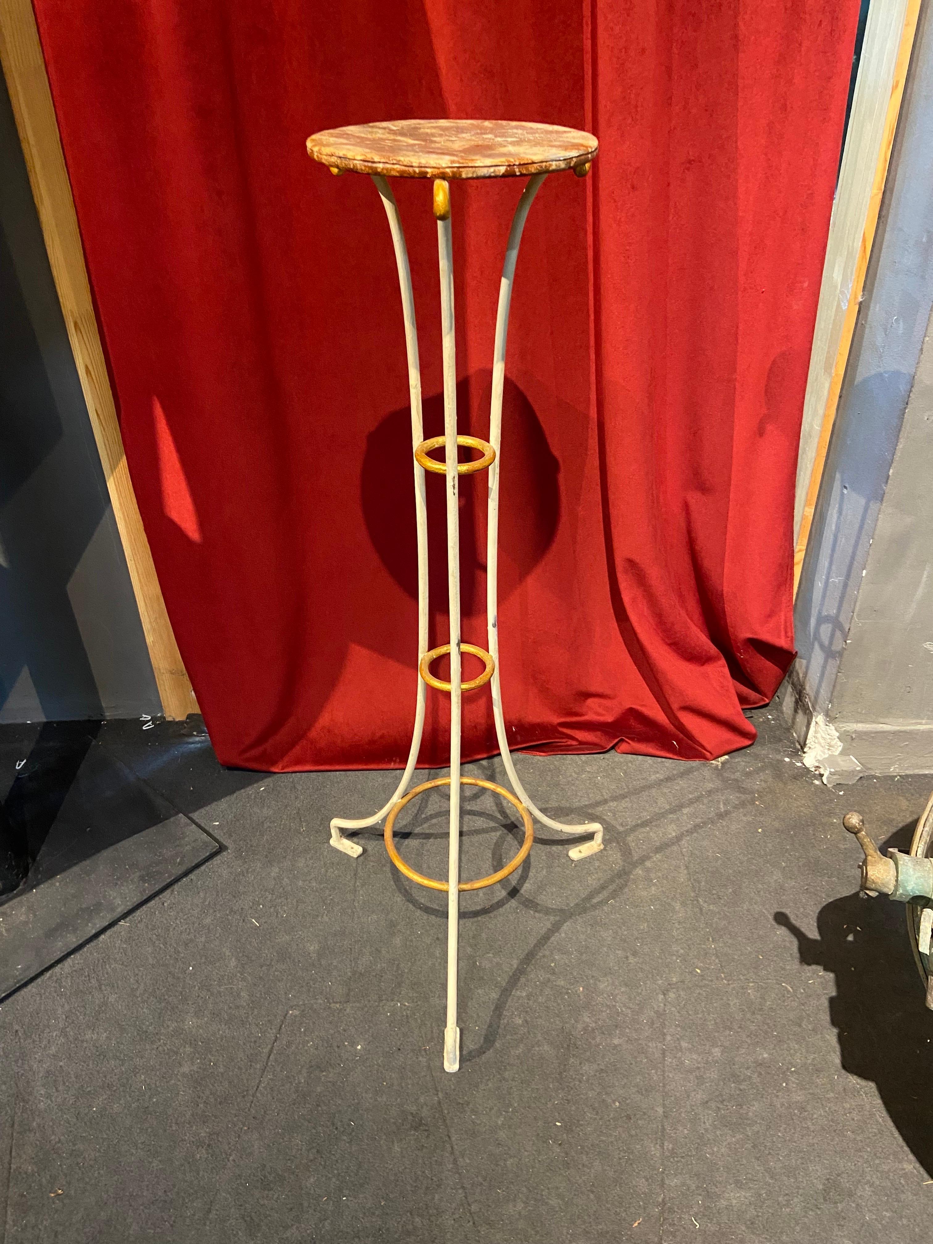 French hand made tall table in cream metal with golden accents at the curved top ends and the rings connecting the structure. The top is also made in metal painted to look like red marble. There is a small hall in the center of the top as this table