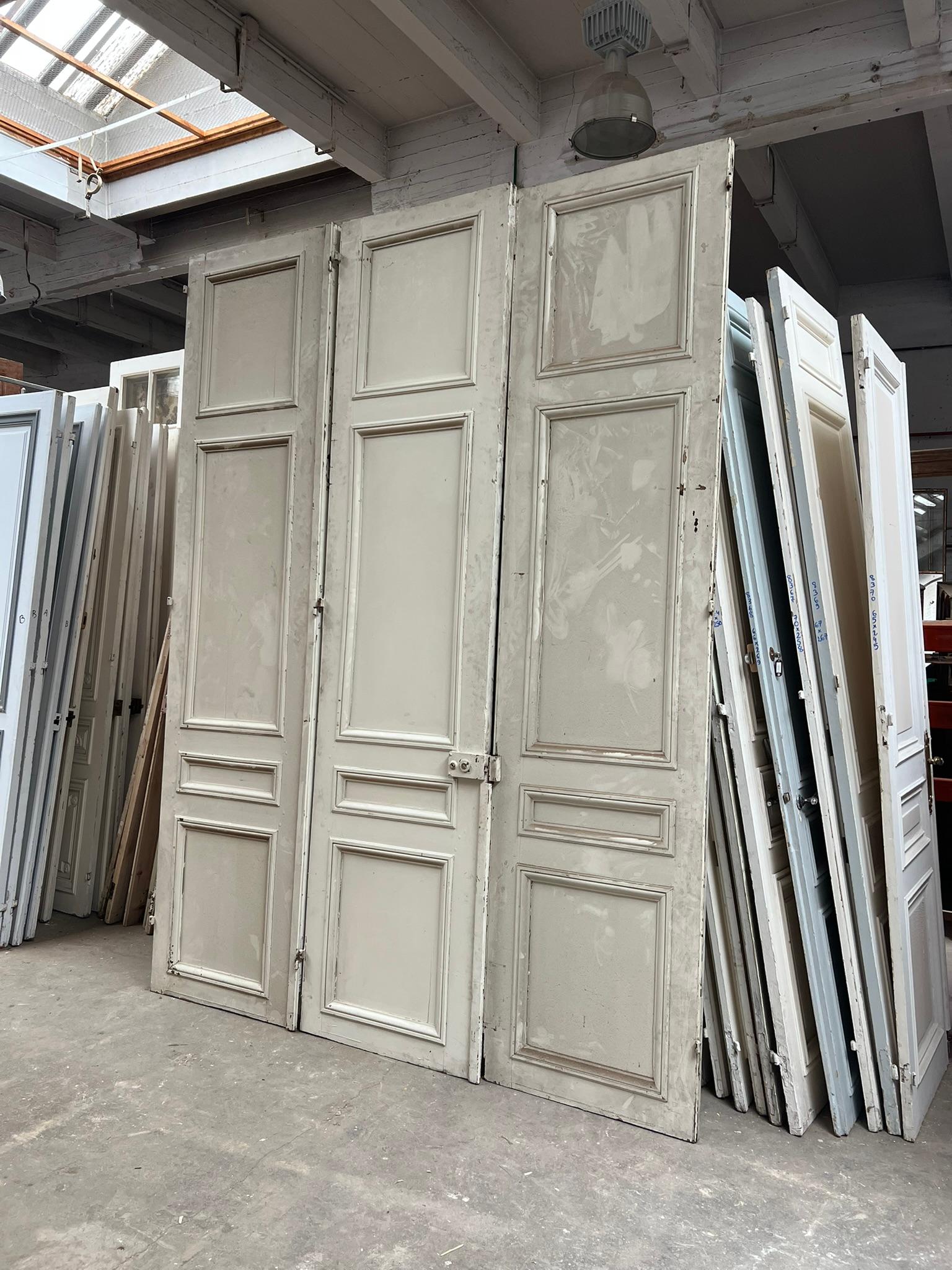 Impressionante trittico di porte francesi haussmanniane risalenti agli inizi del XX secolo. Realizzato in legno e dipinto in bianco sporco, il set presenta pannelli in rilievo modellati tipici dell'architettura parigina della Belle Époque e del