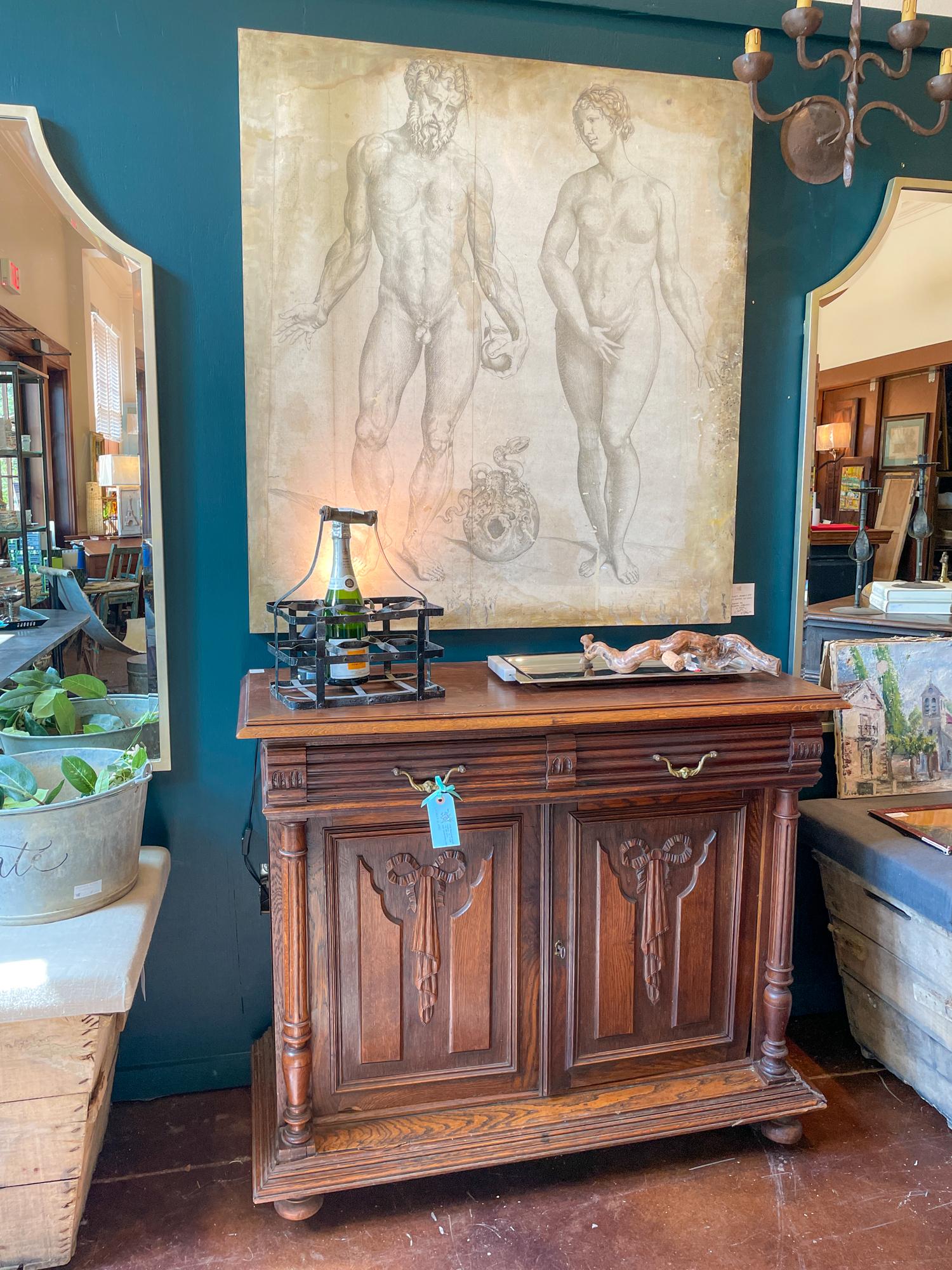 This antique oak carved buffet cabinet was sourced in France and features various carved details, like the large bows on each door, ribbed front drawers, turned side columns and decorative accents. The piece has bun feet at the front which float