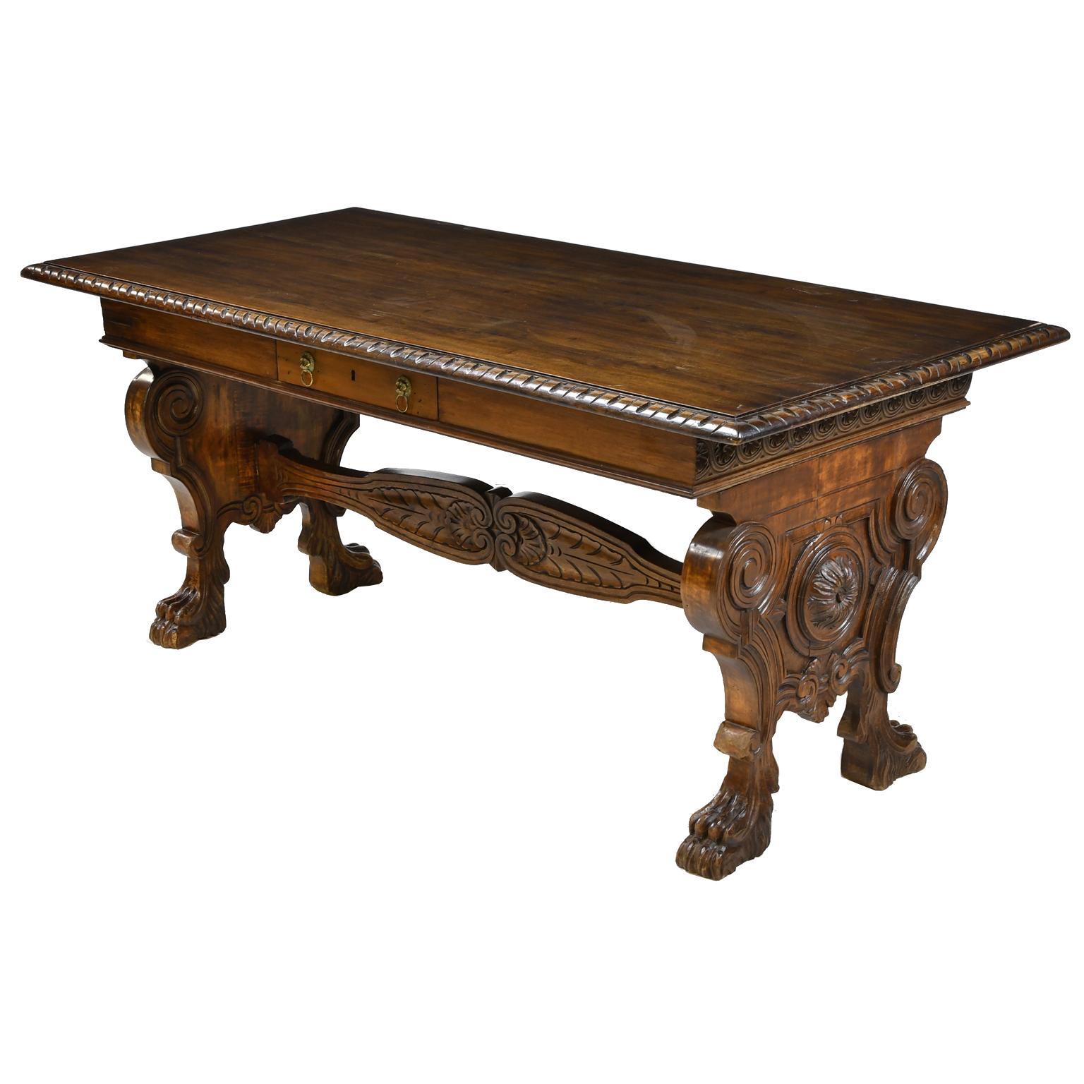 Une très belle table de bibliothèque de style Henri II en noyer avec un plateau rectangulaire sur une base à tréteaux richement sculptée et ornée de volutes, rosettes et fleurs de lys élaborées. La table repose sur des pieds sculptés en forme de