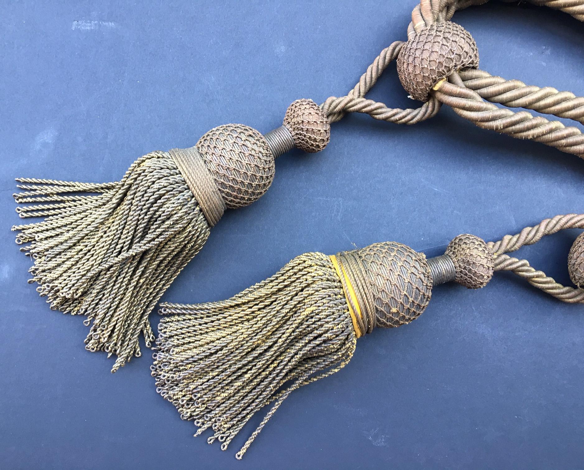 This French antique passmenterie is created, circa 1800. A round netted top is connected with a thick twisted metallic gold bullion rope. This was used as a curtain tieback.

Tassels are seen as far back as biblical times but it is the French who