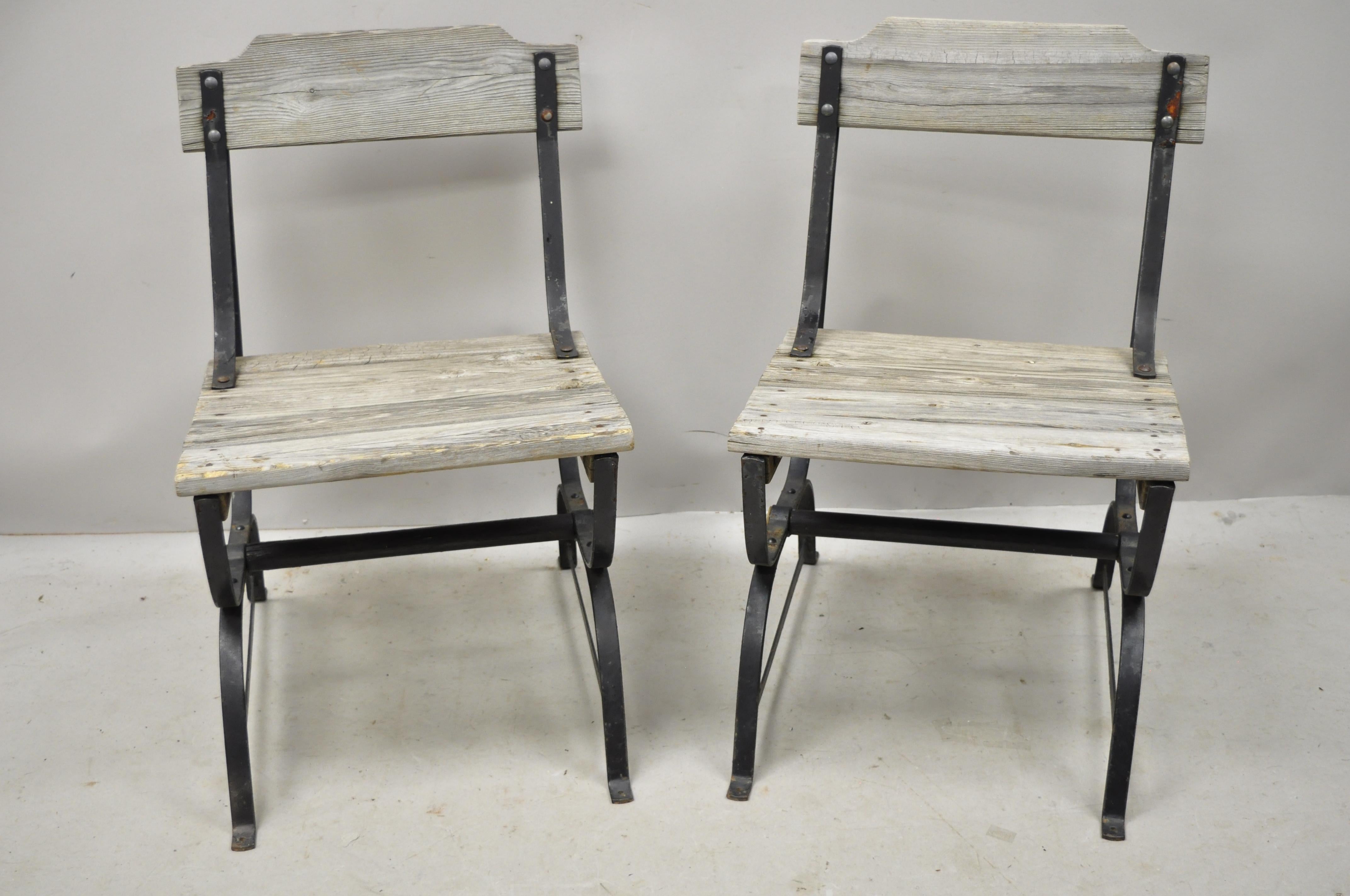 Pair of antique French industrial wrought iron wooden slat seat and back side chairs. Item features wood slat seats and backs, wrought iron construction, wooden stretcher base, distressed finish, very nice antique item, great style and form, circa