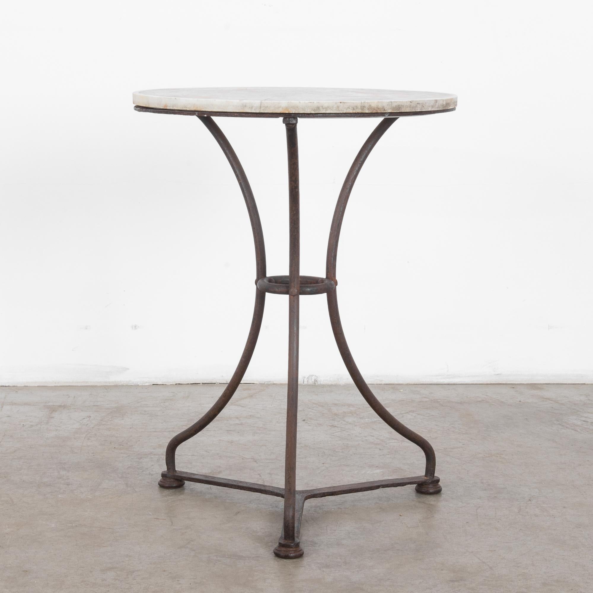 This side table with an elegant three-legged, curved iron frame was made in France. The round, gray-white marble top features variegated patterns and a timeworn patina. This table is an elegant example of the shifts in table design from around the