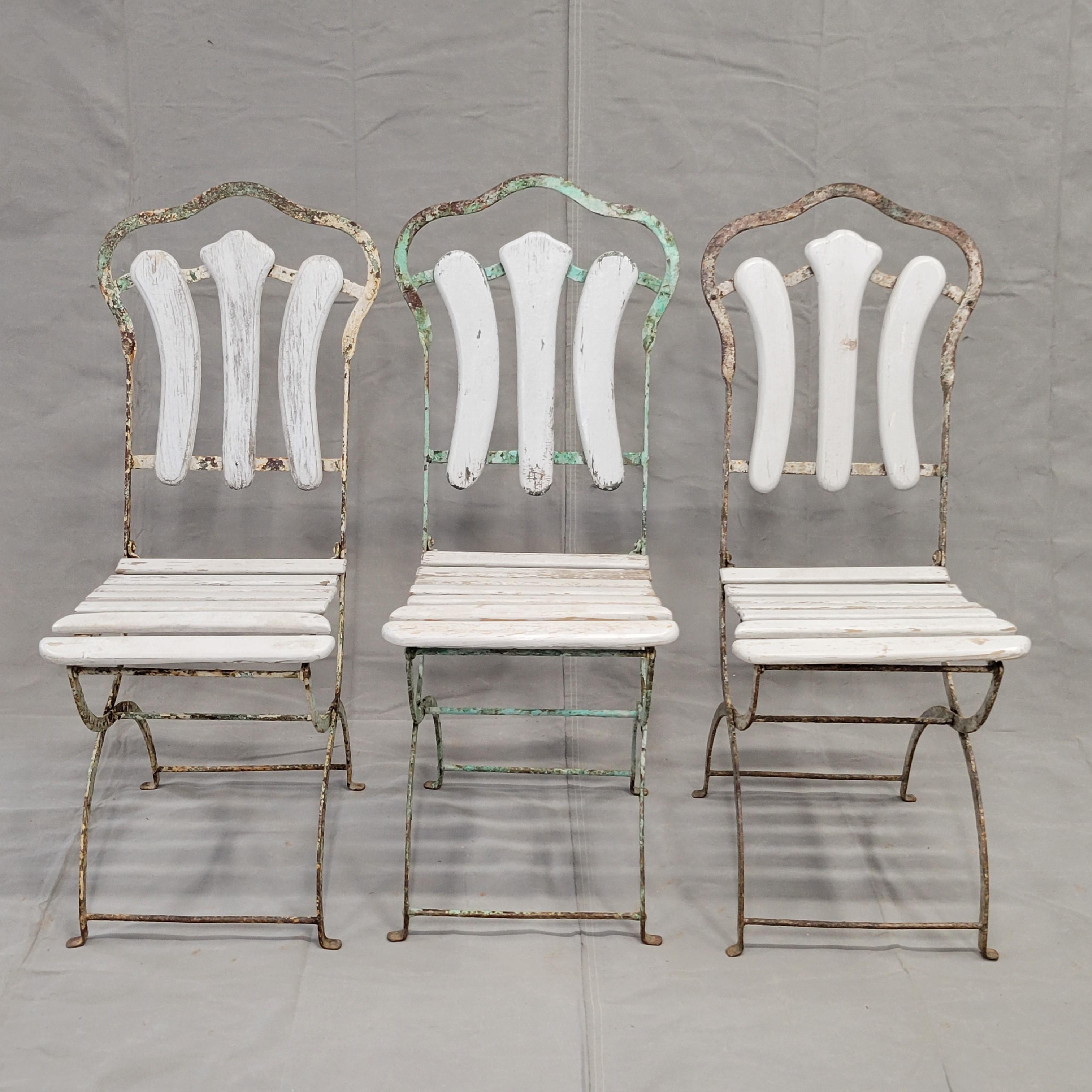 A charming set of antique French iron and wood folding bistro garden chairs. Peeling paint and rust on the iron as well as weathering on the wood lends to the rustic, shabby chic appeal, but they are still strong and very functional. The wood slats