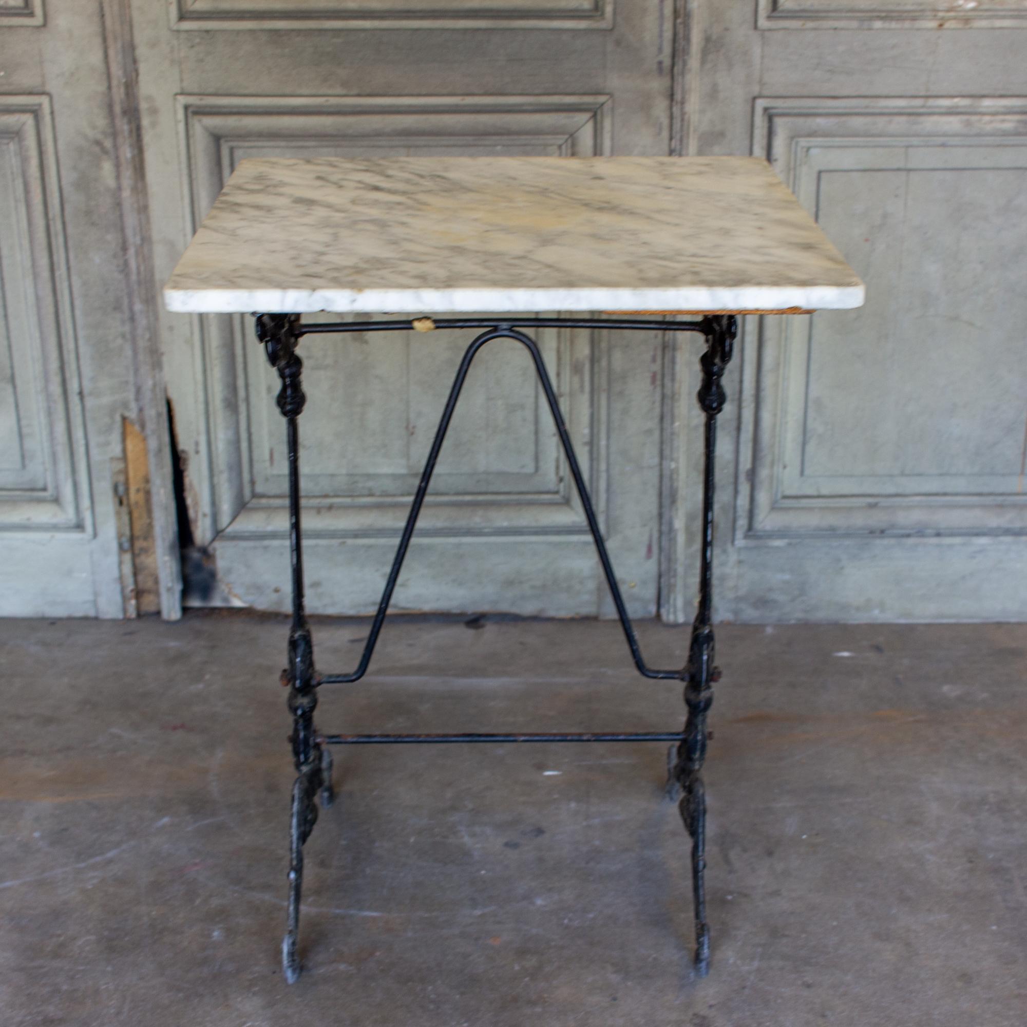 This beautifully decorated bistro table features an iron base with wonderful details and a square-shaped white marble top with rounded corners. The base has scrollwork, floral details and scroll feet. The marble is primarily white with dark gray