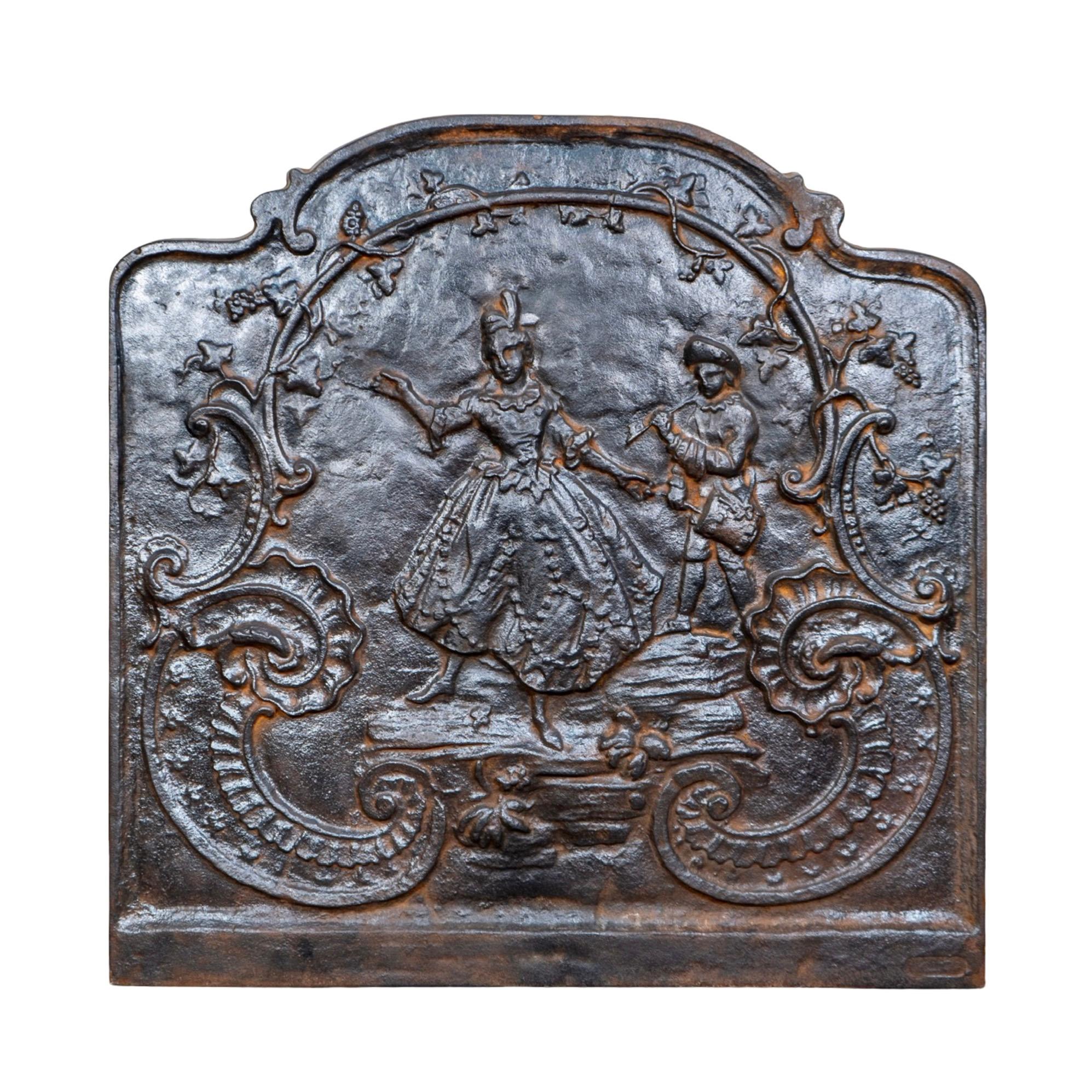 An enchanting 18th-century French cast iron fireback showcasing a romantic Rococo tableau in delicate relief. The scene depicts a finely dressed couple in period attire—the woman in a voluminous gown with lace-like detailing and the man in a tunic