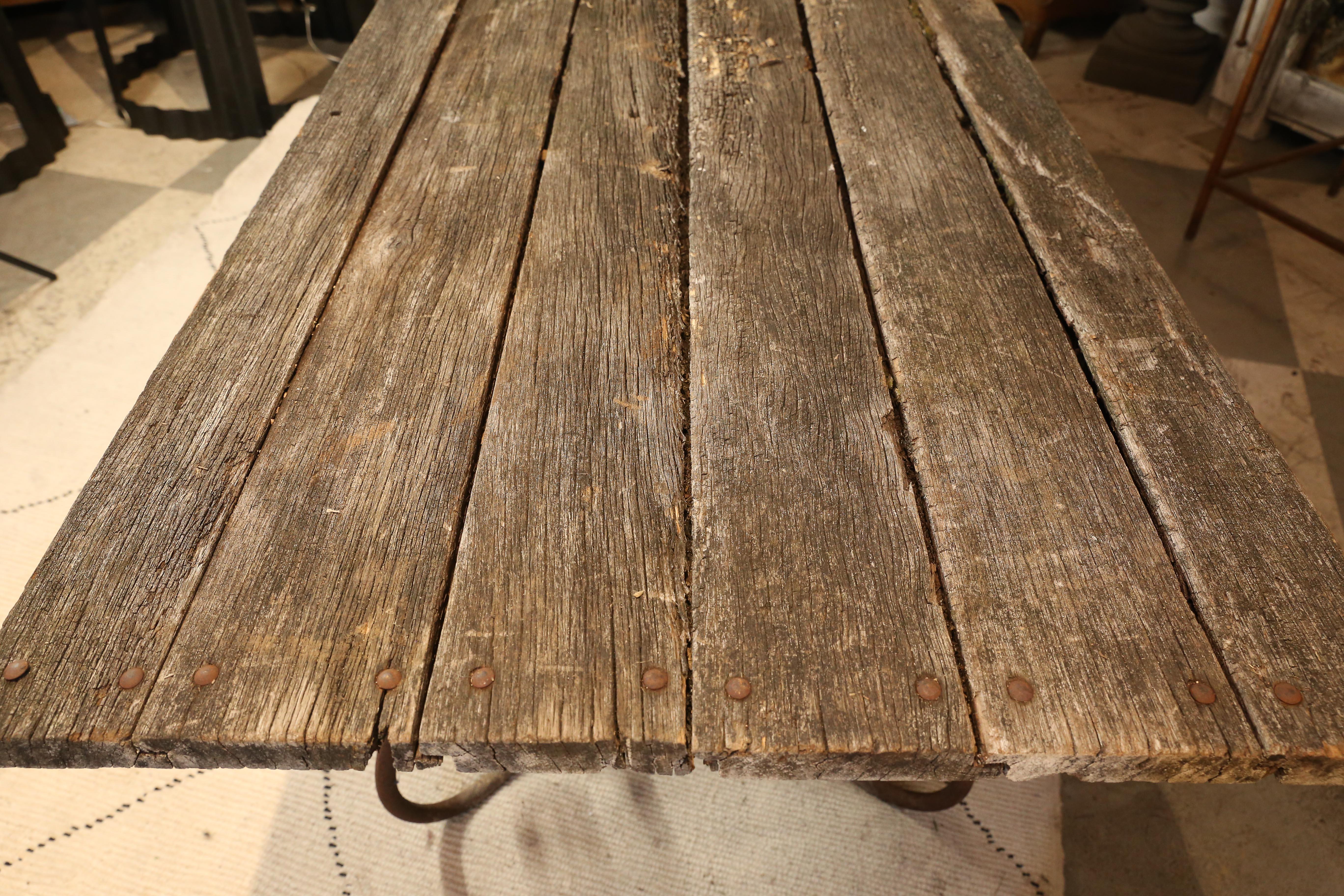 This antique garden table has a solid iron base and lovely distressed, wooden top consistent being in an old French garden where it was discovered. Beautiful and rustic, the handmade base features curved feet and has developed rust throughout, which
