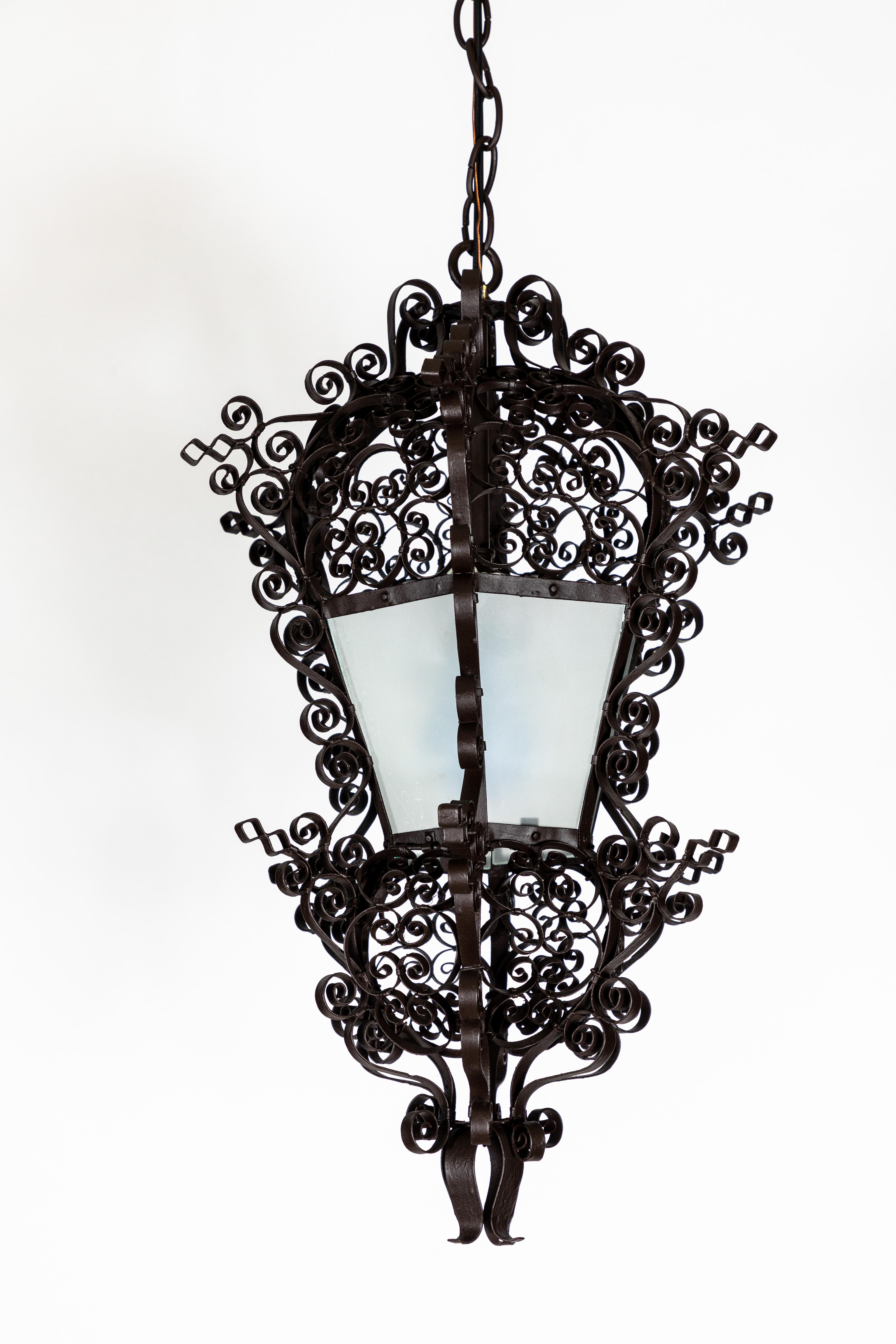 A fanciful lantern imagined in iron, this antique French iron hanging pendant light made up of elegant ornate curl detailing and a mid-section that illuminates is as interesting off as it is on. This piece has been newly restored in a polished